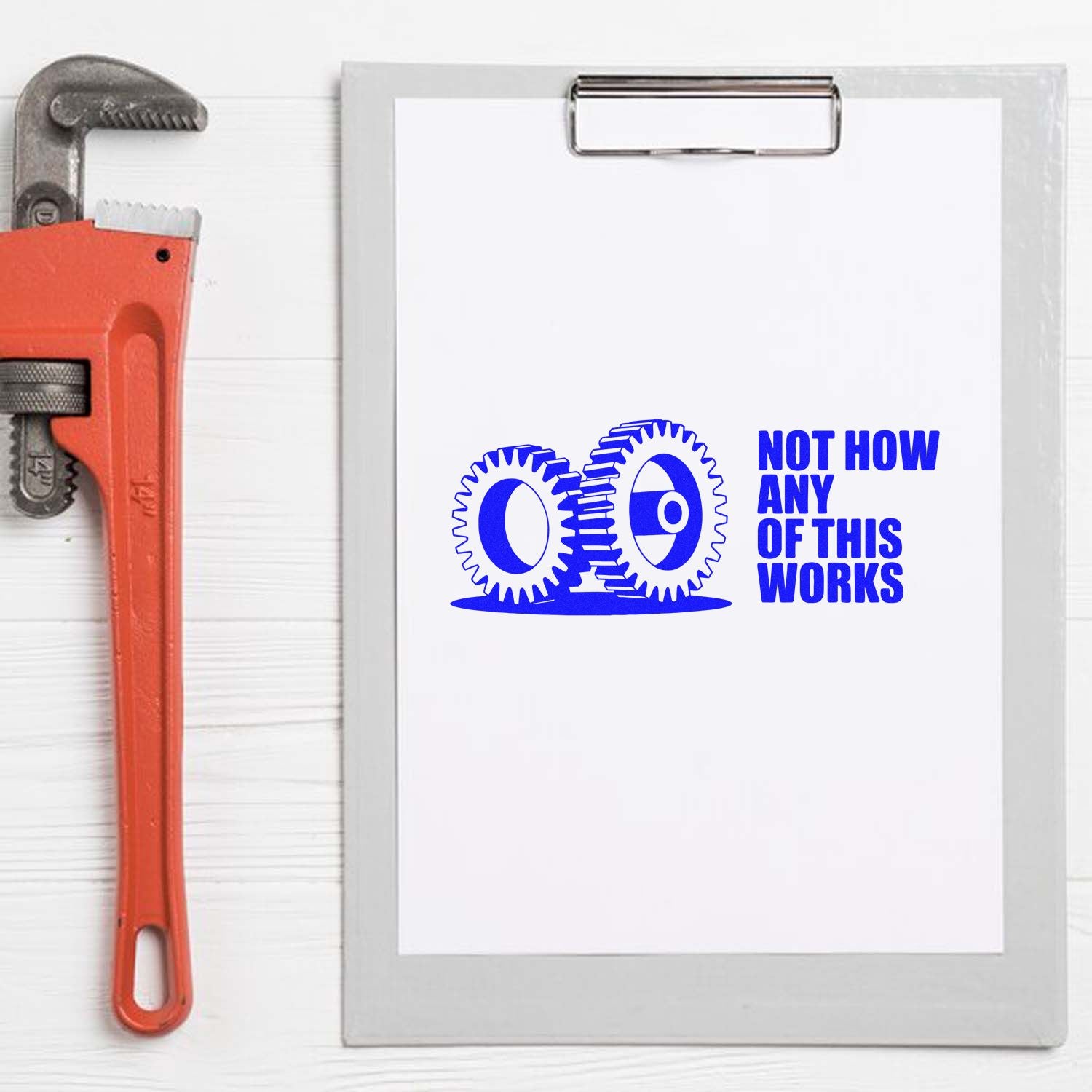 Blue rubber stamp seal on clipboard with gears and NOT HOW ANY OF THIS WORKS; red pipe wrench at left.