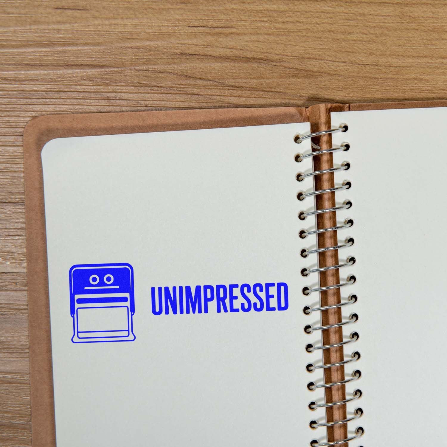 Blue UNIMPRESSED stamp and seal on a white spiral notebook page over a wood table