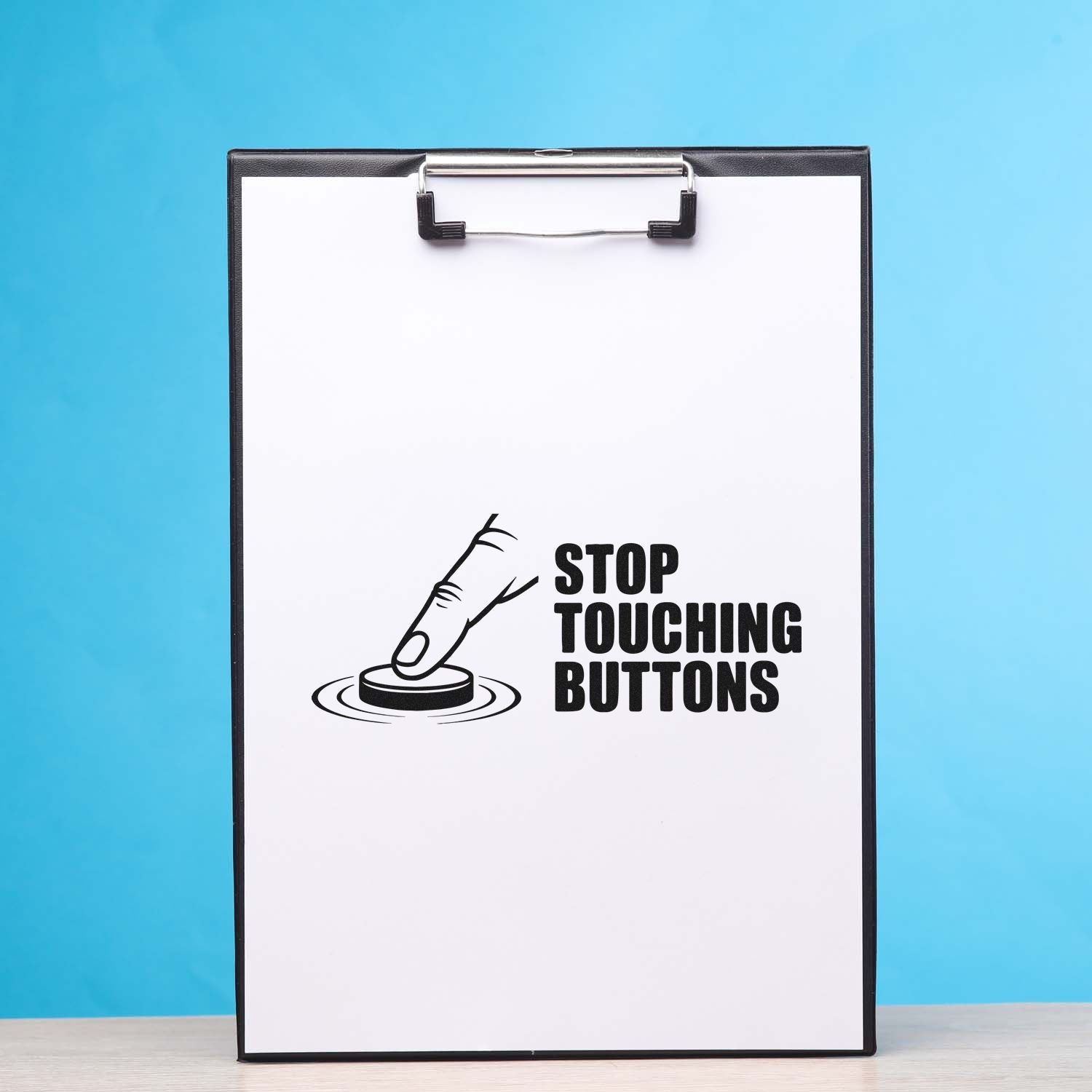 Black clipboard-style stamp and seal product with white sheet, blue background, and STOP TOUCHING BUTTONS warning graphic.