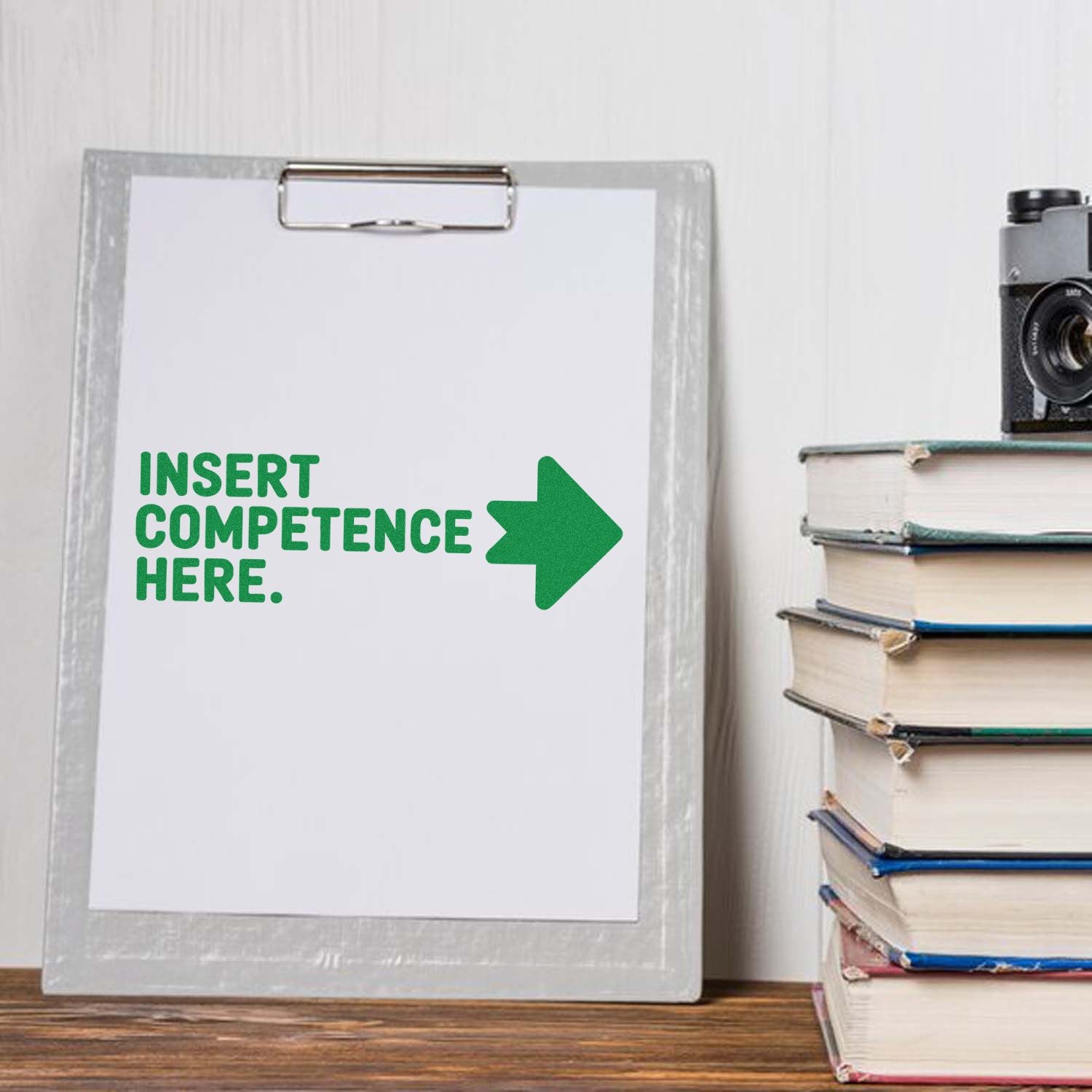 Custom stamp and seal sample on white clipboard, green INSERT COMPETENCE HERE text and arrow beside stacked books.