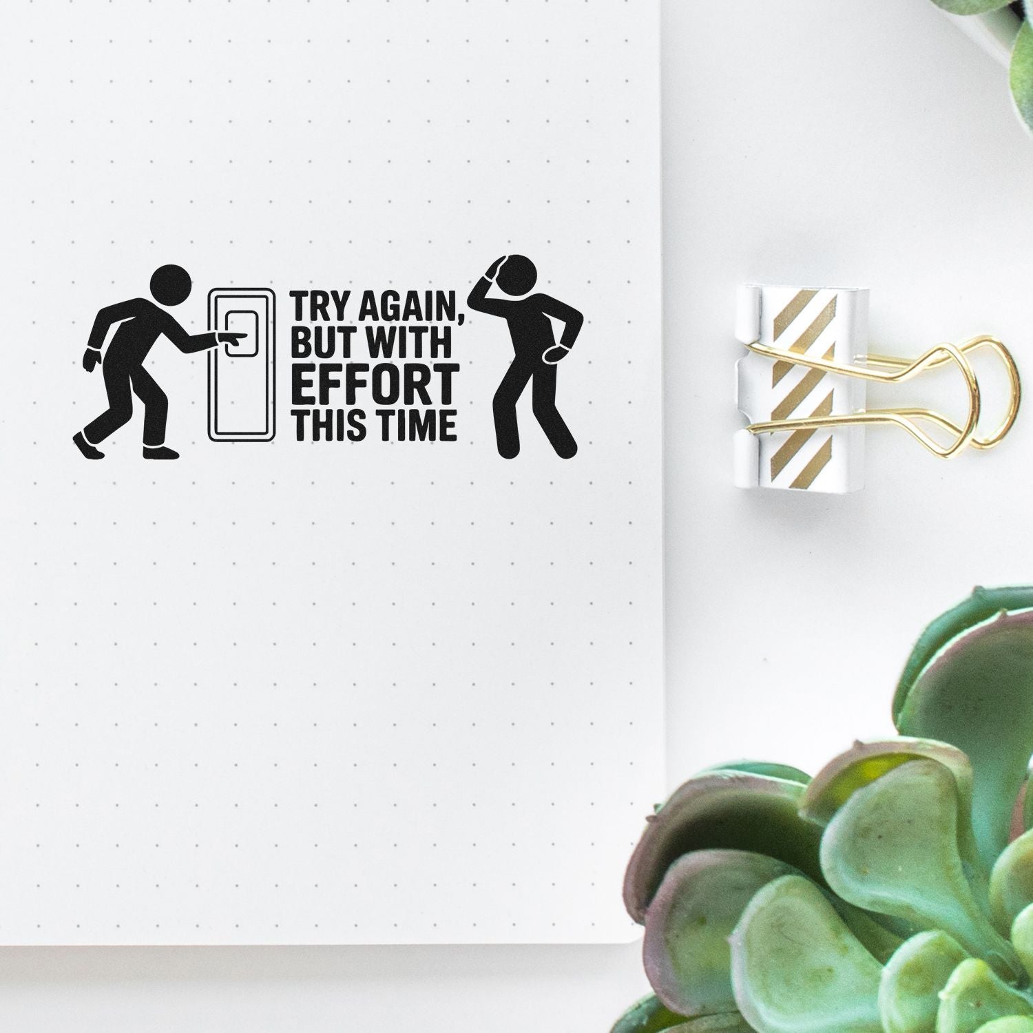 Black motivational stamp on dotted white notebook page, with a gold-striped paper seal clipped by a gold binder clip.