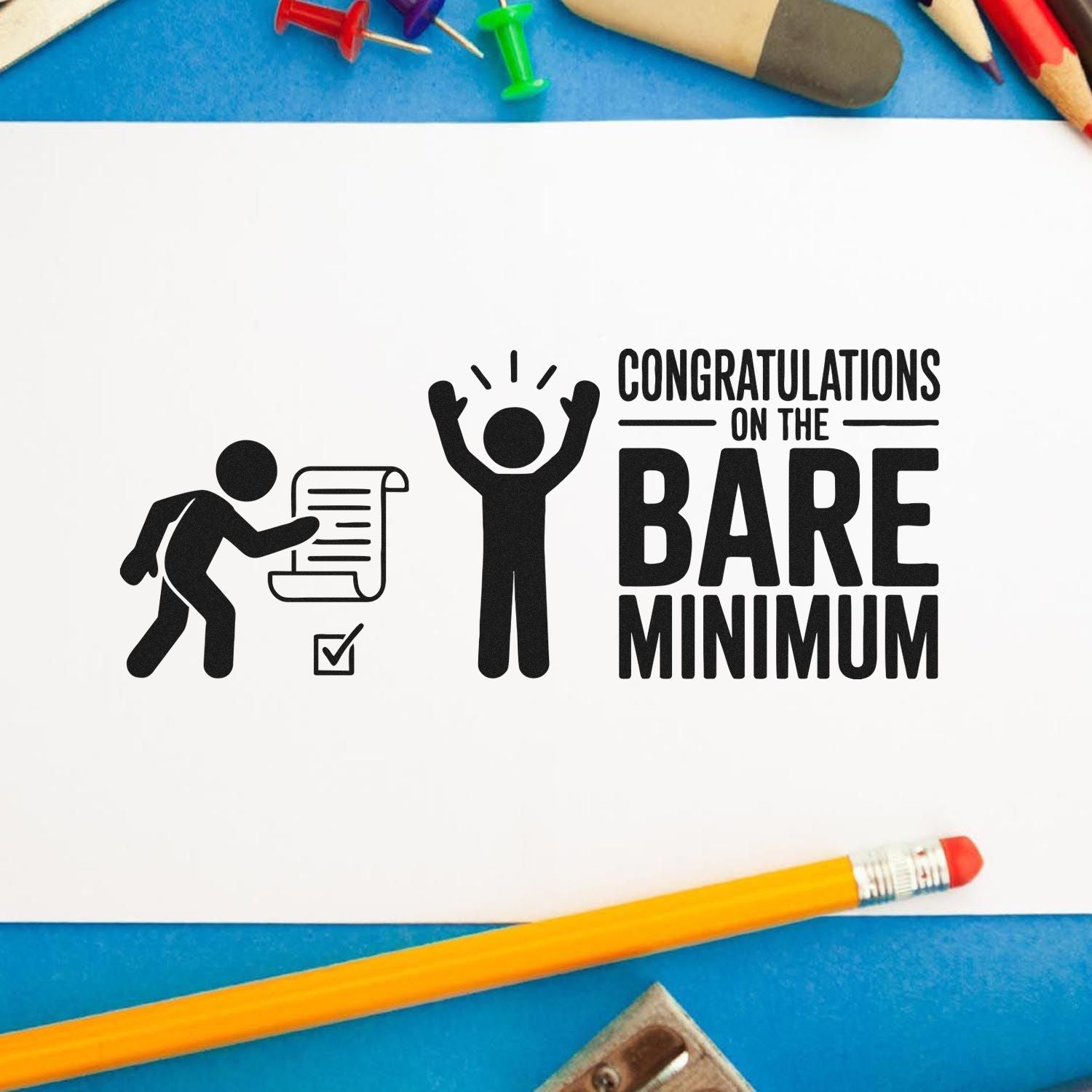 Black stamp seal reading Congratulations on the Bare Minimum with stick figures on white paper, blue background, and pencils.