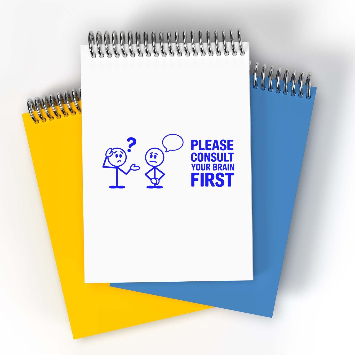 Blue custom stamp and seal on white spiral notebook reading Please consult your brain first, with yellow and blue notebooks behind.