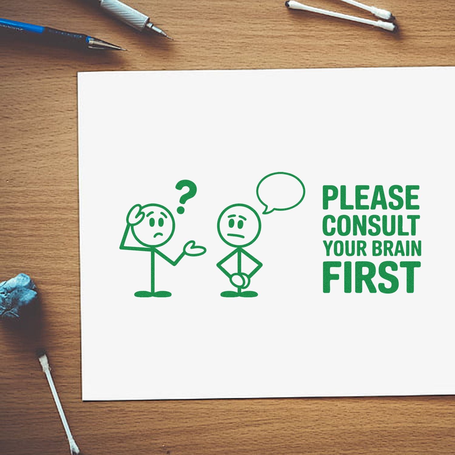 Green stamp/seal design on white paper with two stick figures and Please Consult Your Brain First in green on a wood desk.