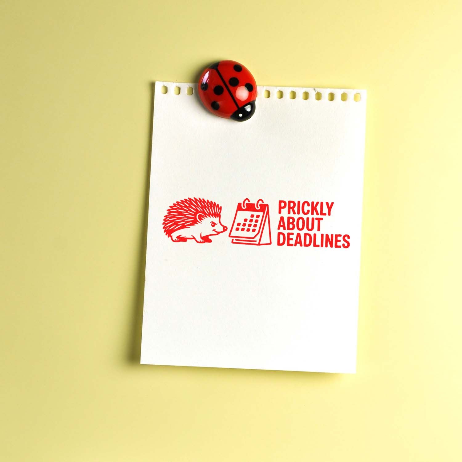 Red stamp seal with hedgehog and calendar reading Prickly About Deadlines on a white notepad, topped by a red ladybug, on yellow.