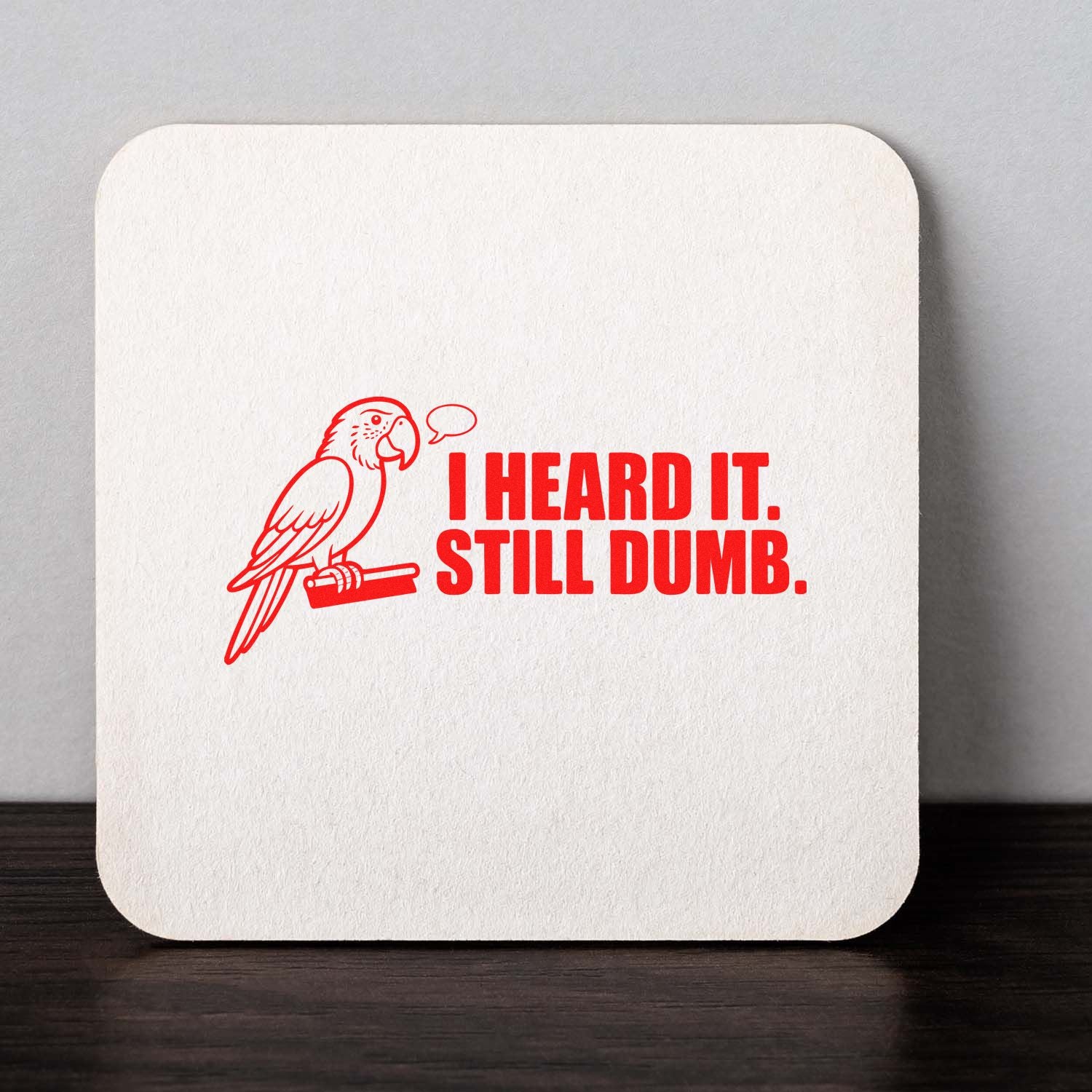 Red parrot stamp seal on white textured square coaster with bold text: I HEARD IT. STILL DUMB.