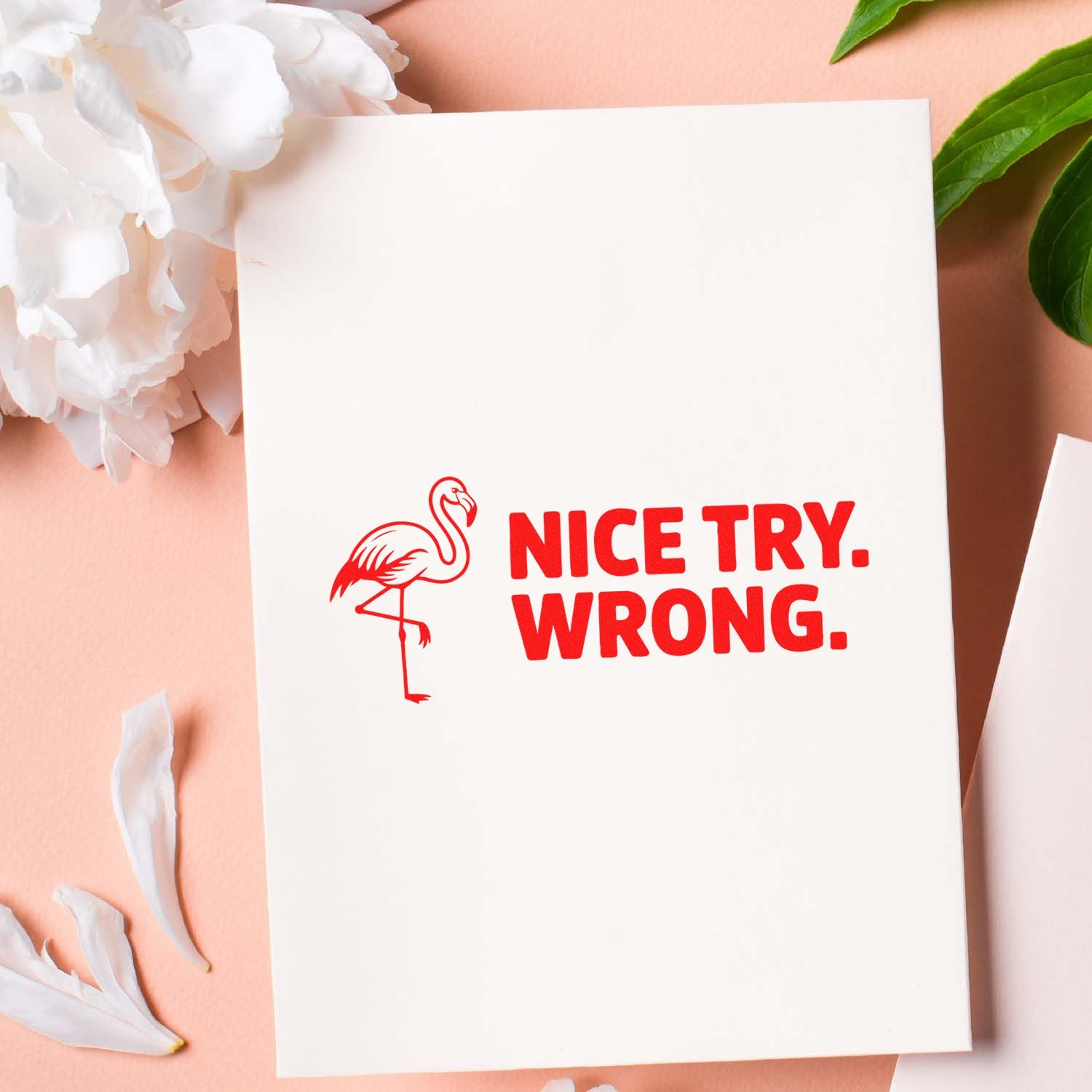 Red flamingo stamp and seal with NICE TRY. WRONG. on white card, set on a peach background with white flowers and green leaves.