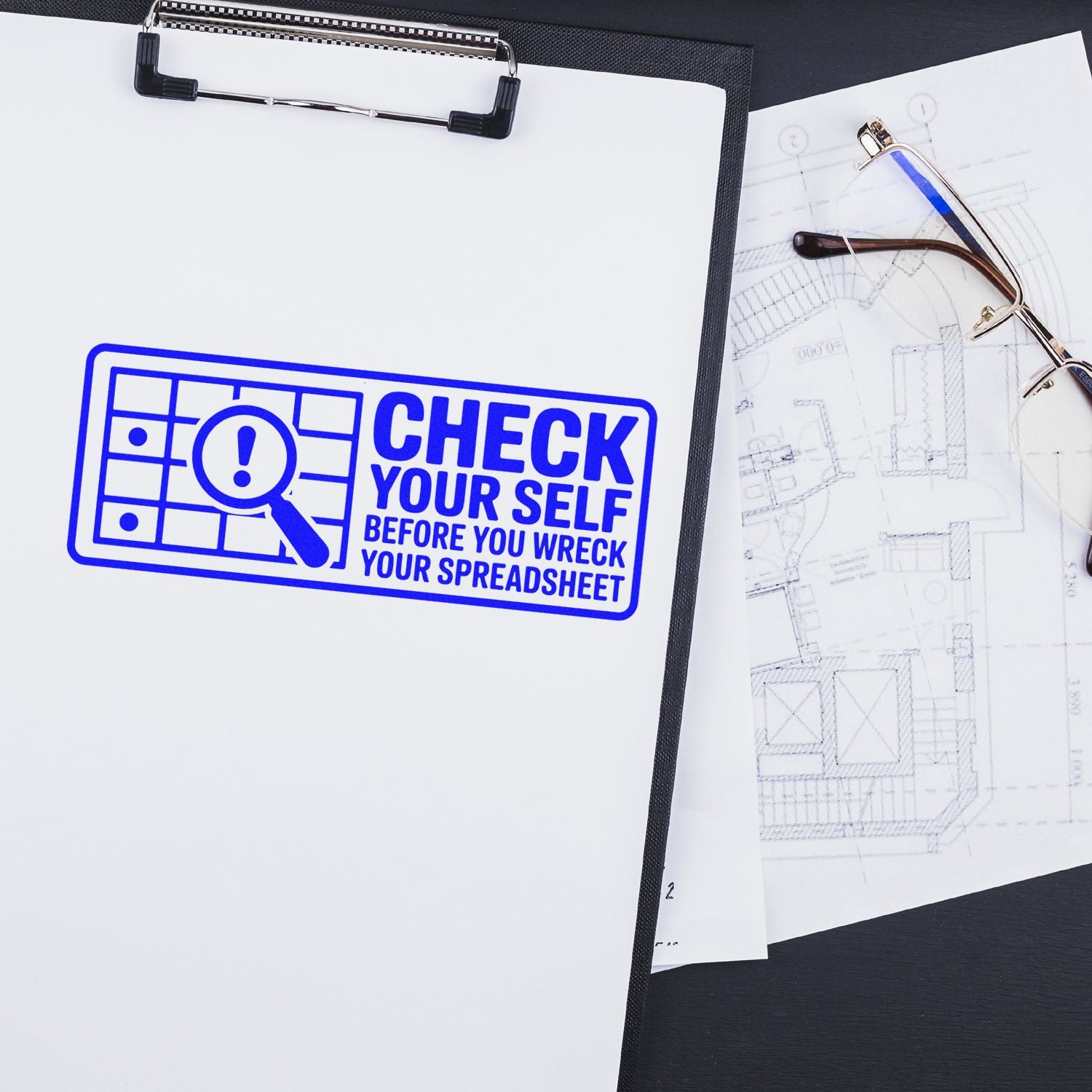 Blue rubber stamp/seal on clipboard reading Check Yourself Before You Wreck Your Spreadsheet, beside eyeglasses and plans.