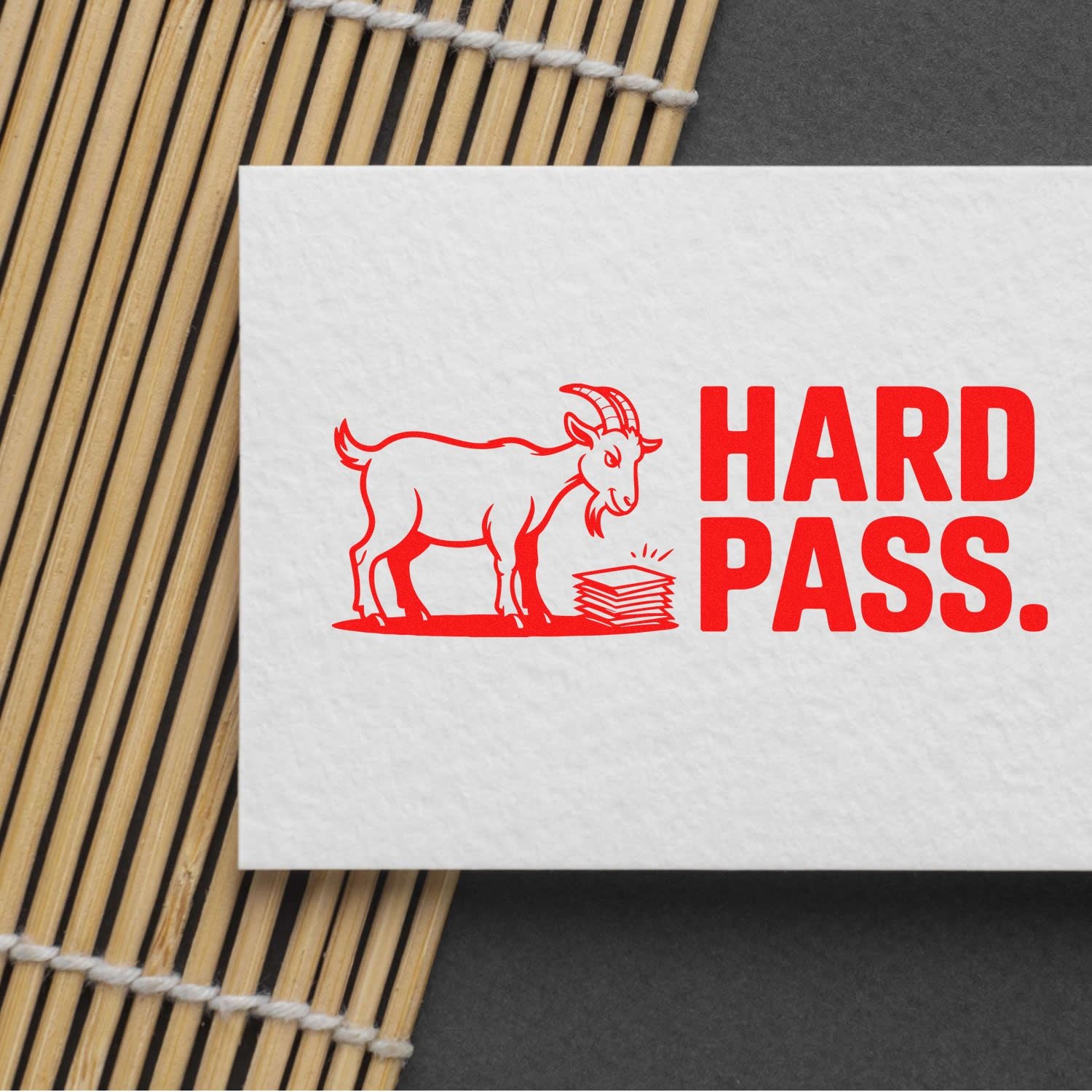 Red stamp and seal design with goat and HARD PASS in bold red on white paper over a bamboo mat.