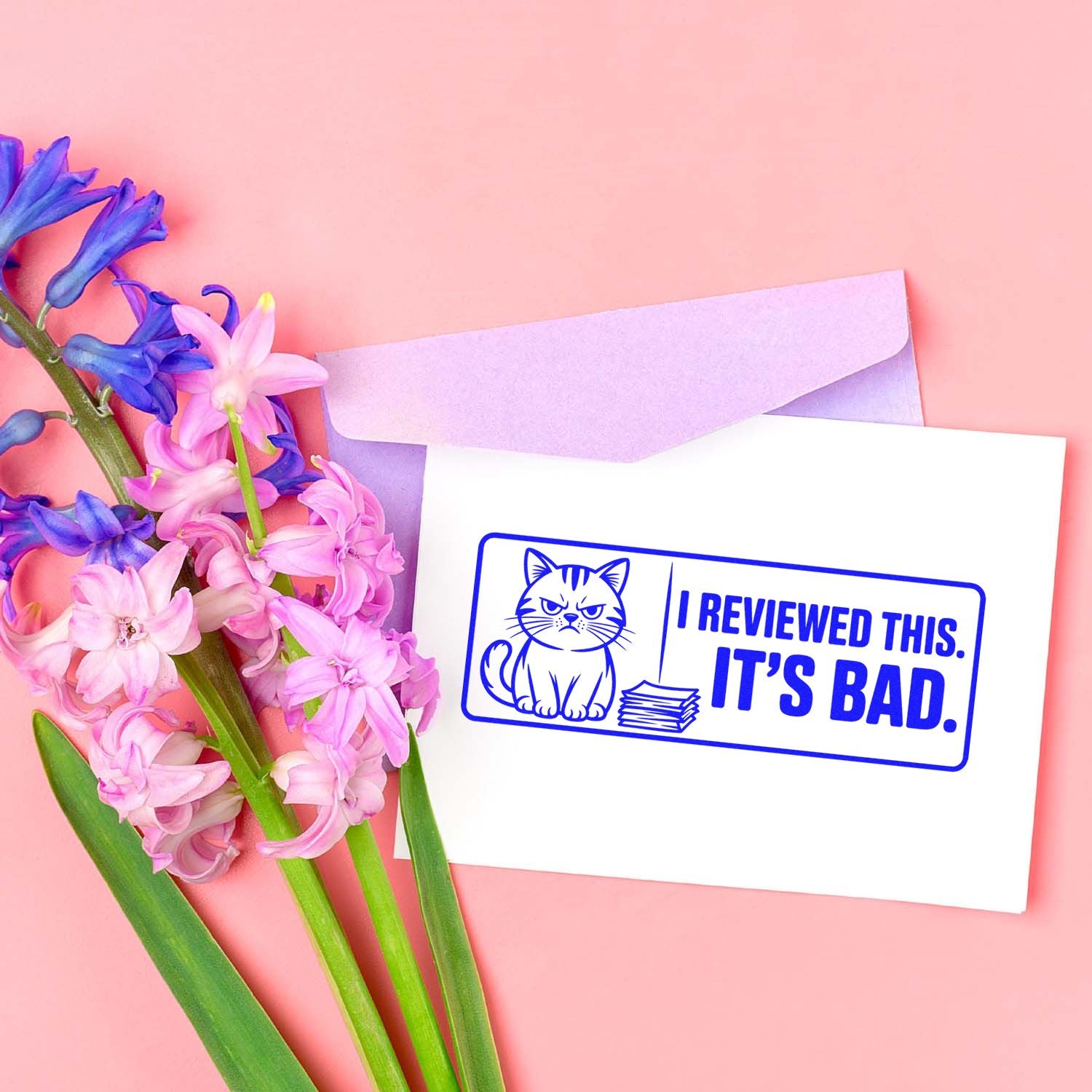 Blue cat rubber stamp reading I reviewed this. Its bad. on white card, with lavender envelope and pink-purple flowers on pink.