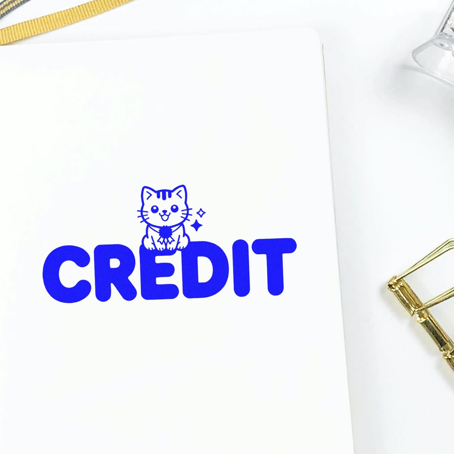 Blue CREDIT stamp and seal with a cute cat icon on white paper, accented by gold binder clips.