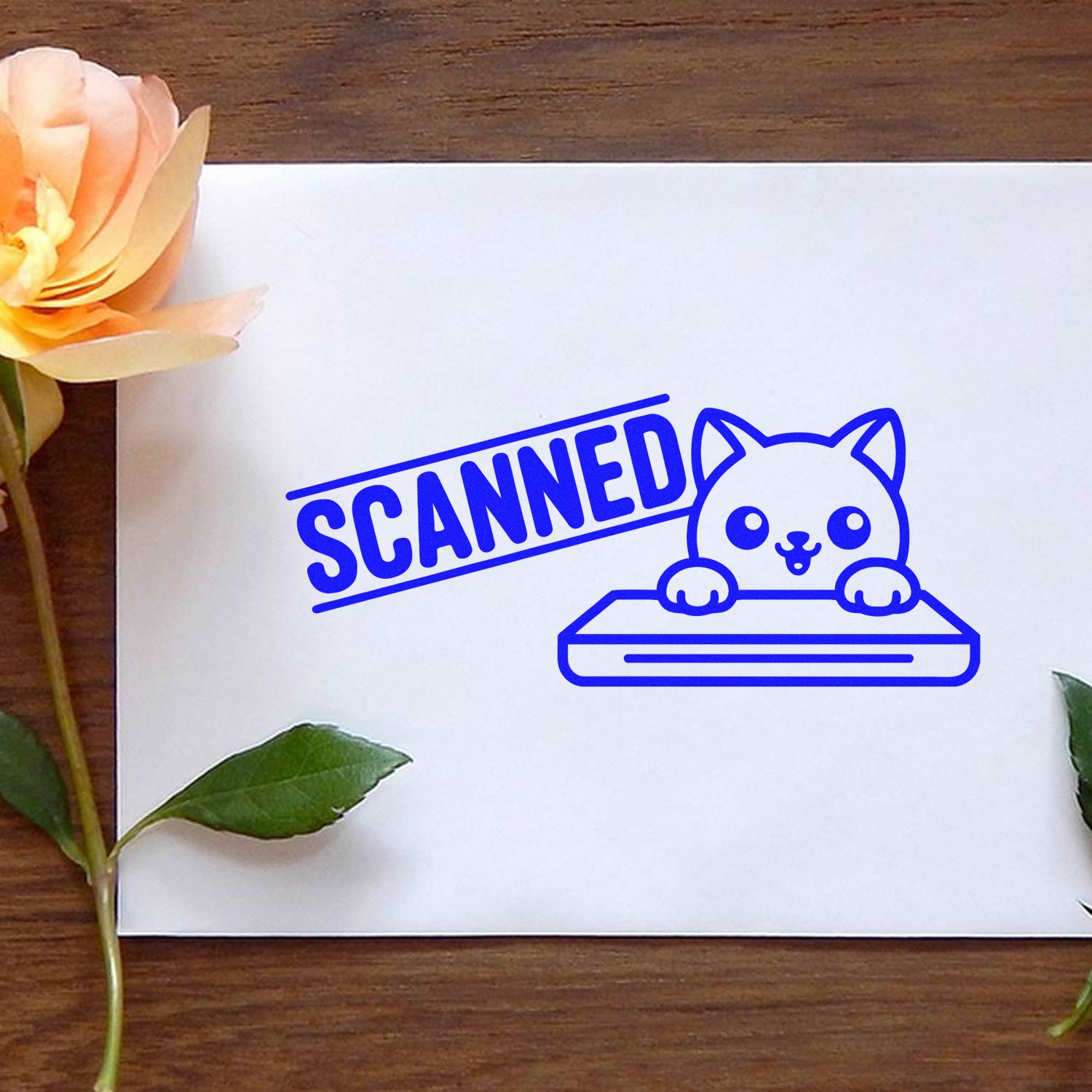 Blue SCANNED rubber stamp with cute cat seal on white paper, accented by peach flower and green leaves on a wood desk.