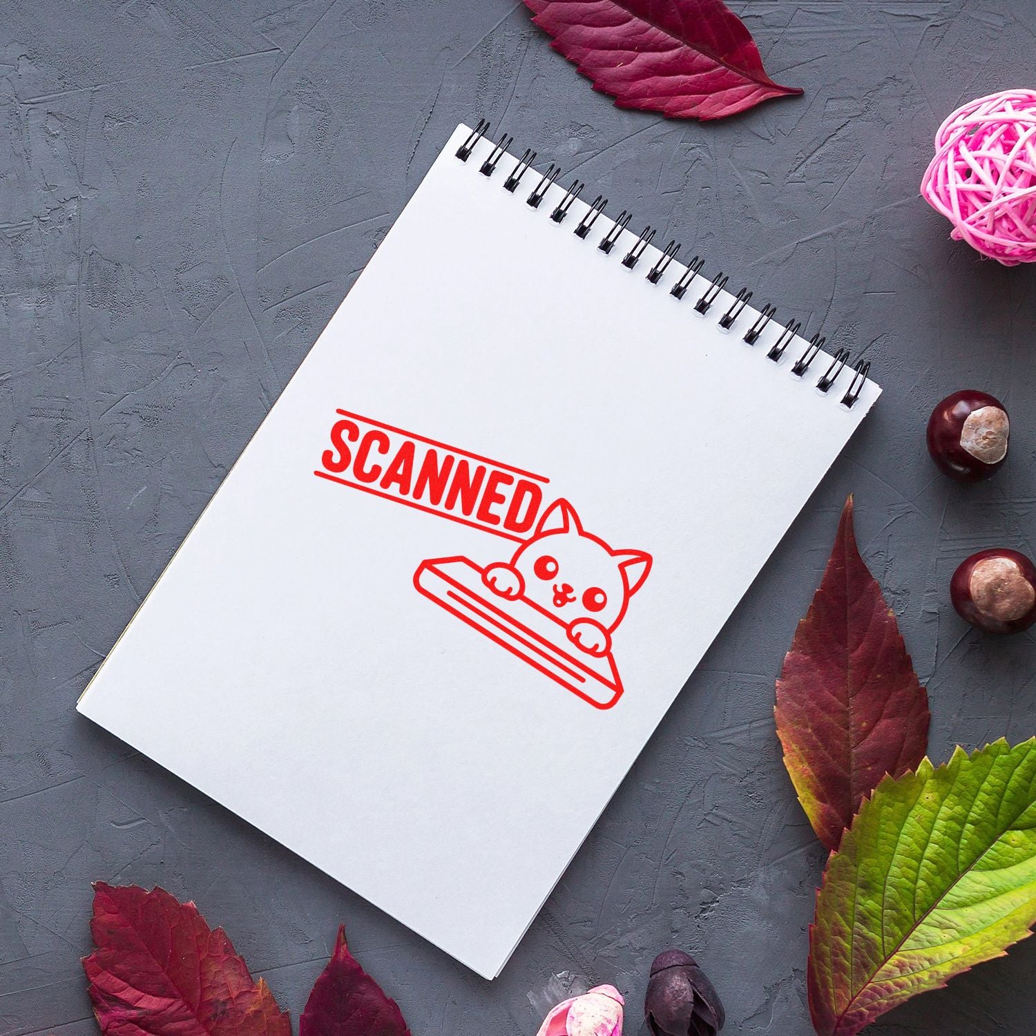 White spiral notebook featuring a red SCANNED cat stamp and seal, with gray background, autumn leaves, and pink accents.