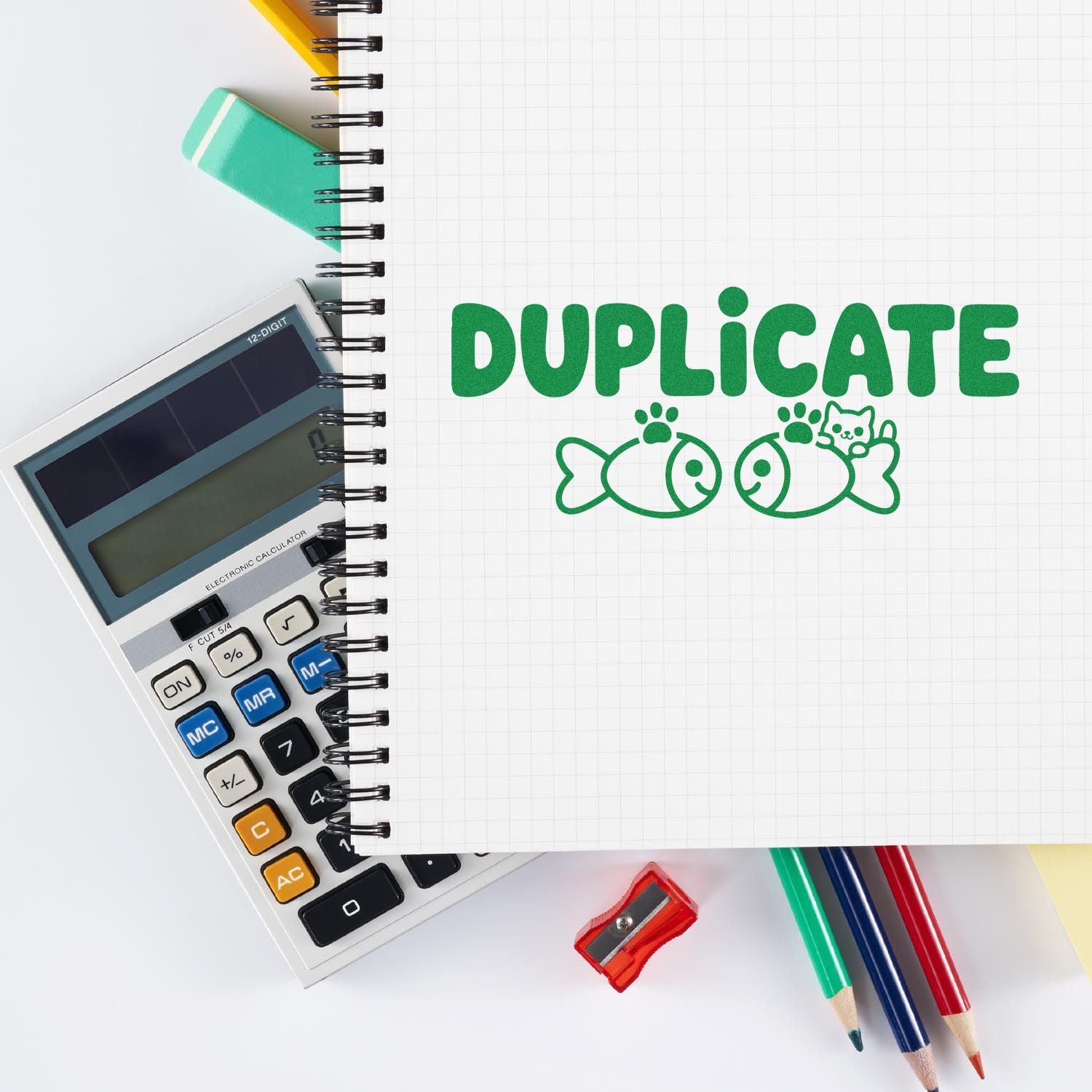 Green DUPLICATE stamp seal on graph notebook, with calculator, pencils and sharpener on white desk.