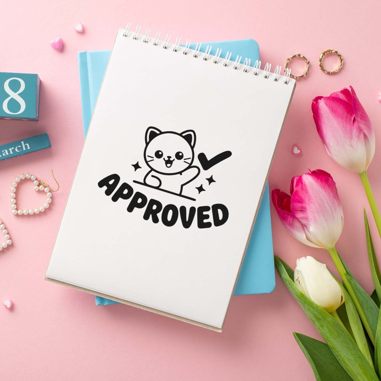 Cat APPROVED stamp and seal design on white spiral notebook, with pink tulips and pastel blue stationery on a pink background.