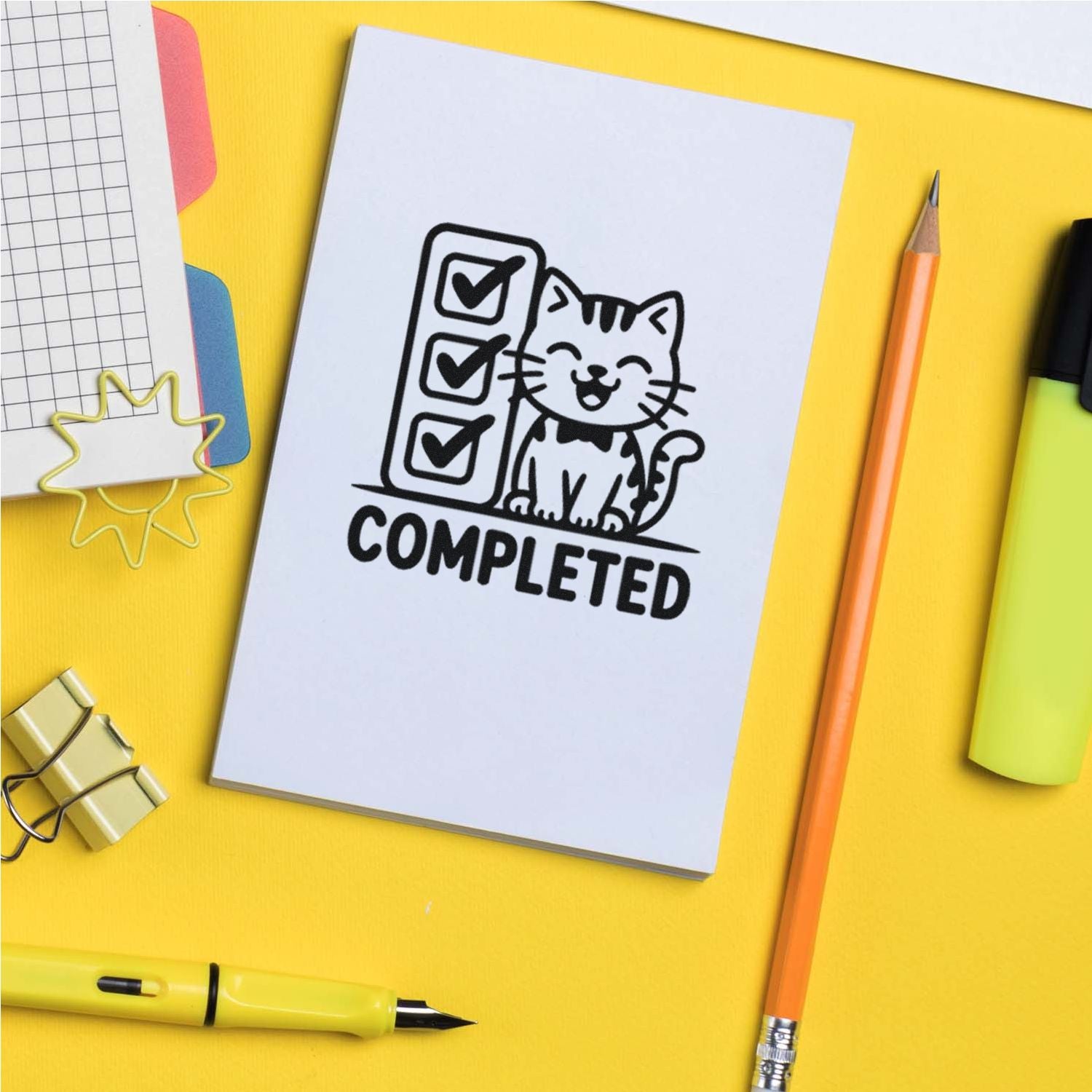 Cat checklist COMPLETED rubber stamp on white paper, with yellow desk, pencils, highlighter and office supplies.