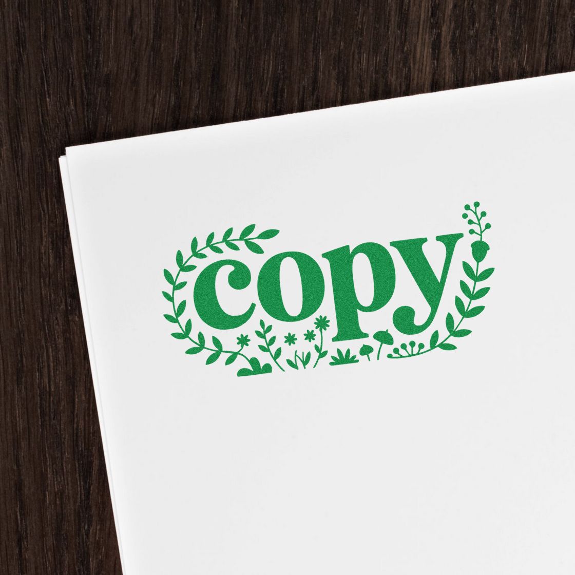 Green copy stamp seal with leafy wreath on white paper on dark wood background.