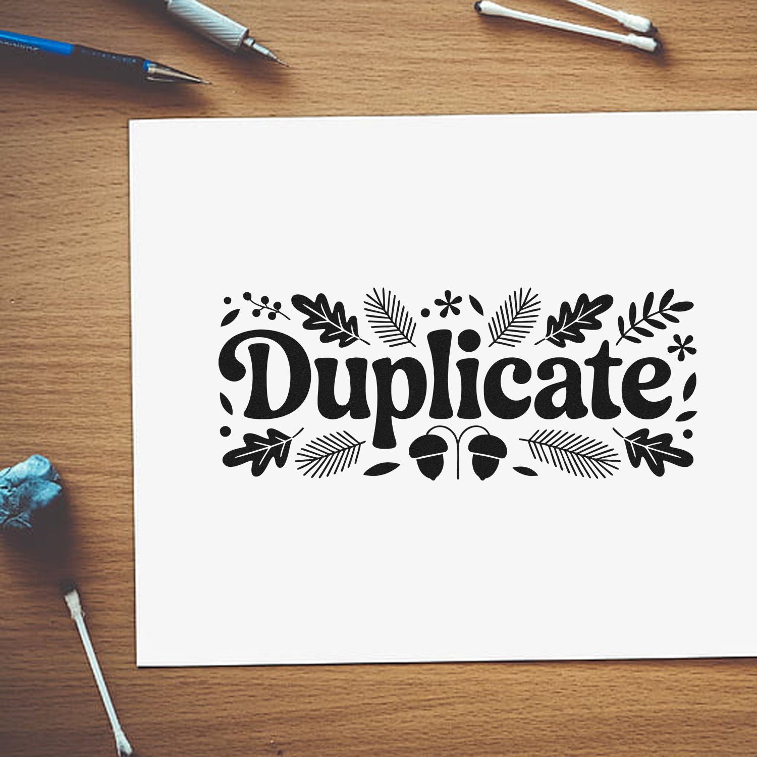 Black decorative duplicate stamp seal with botanical leaf accents on white paper, on a wood desk.