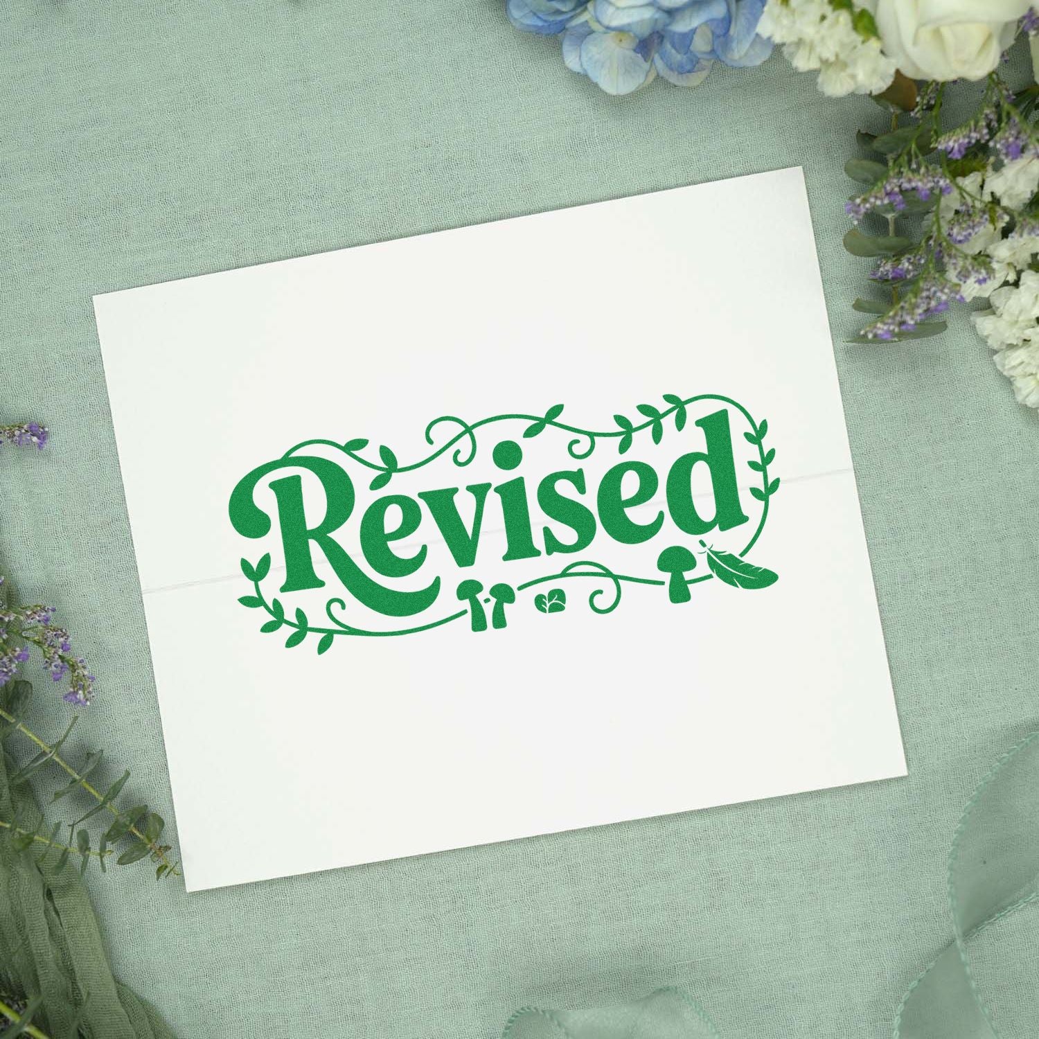 Green Revised stamp seal with leafy border on white card, on mint fabric with pastel flowers.