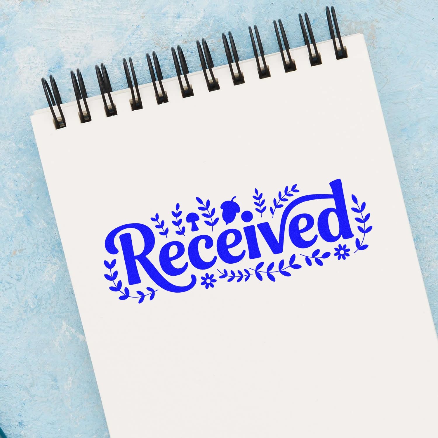 Blue Received stamp and seal design on a white spiral notepad with floral leaves, against a light blue textured background.