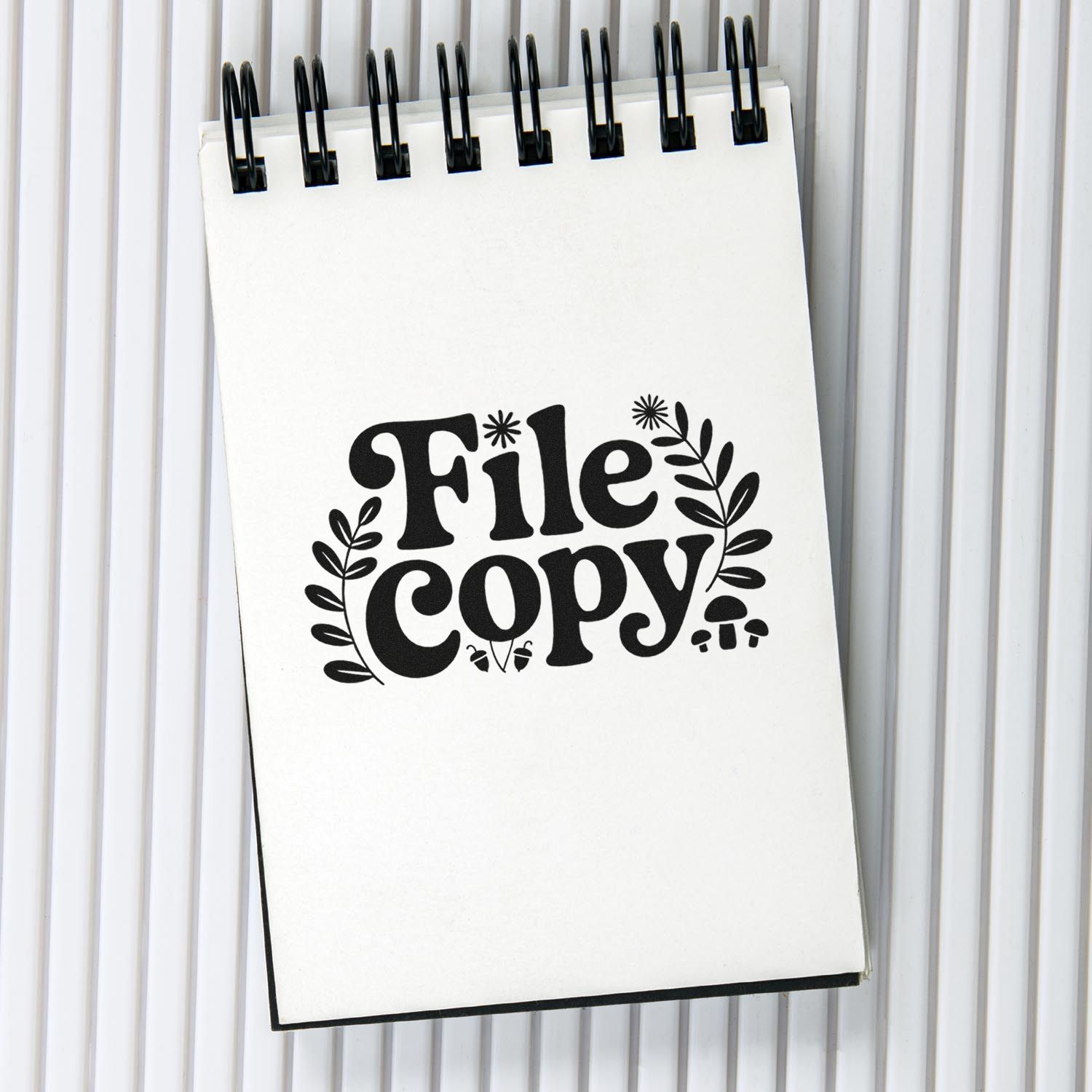 Black File Copy stamp and seal design with leafy accents on a white spiral notebook