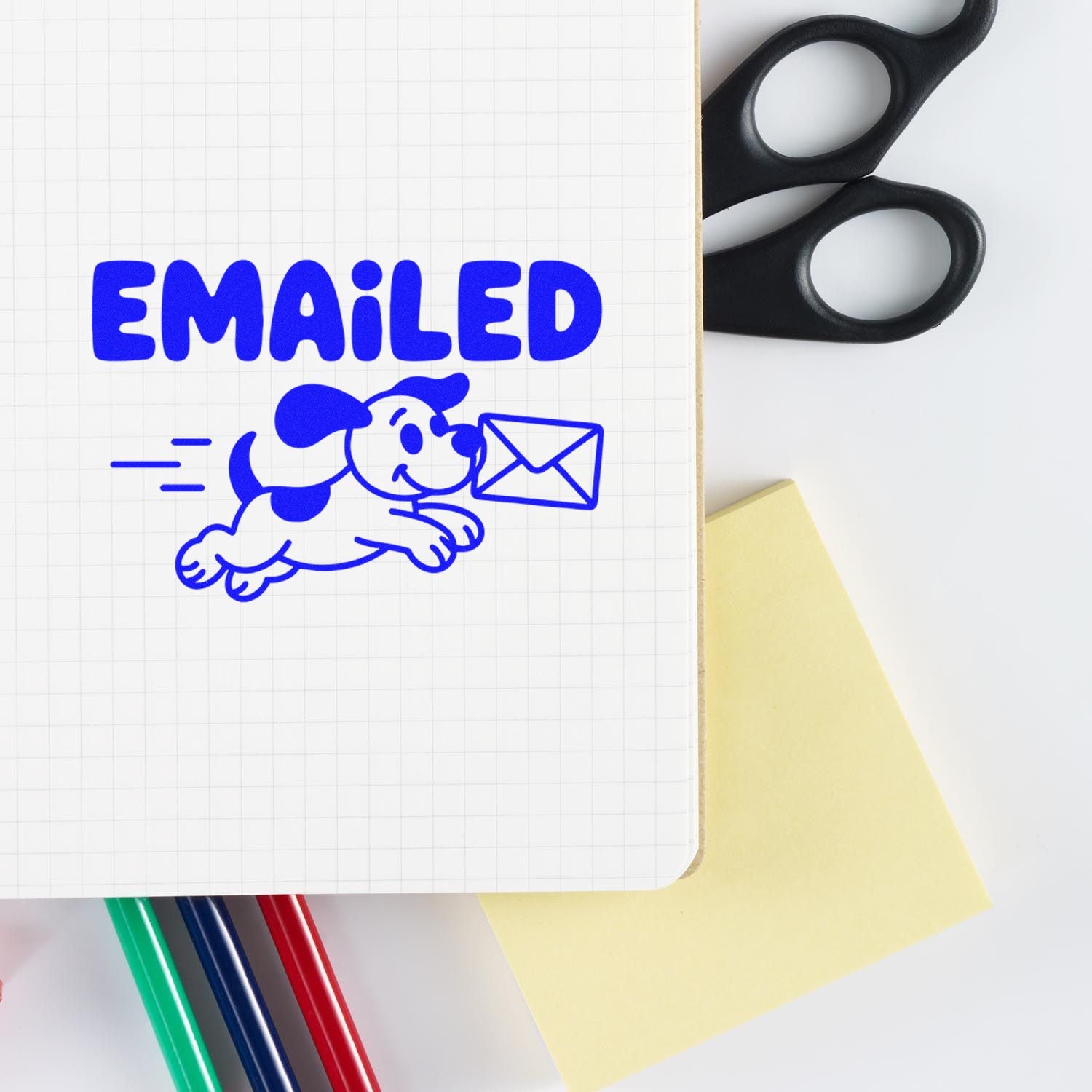 Blue EMAILED stamp and seal design with dog carrying envelope on grid paper, plus black scissors, yellow note, and colored pens.