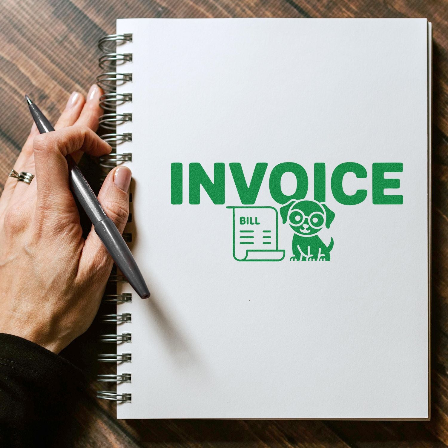 Green invoice stamp and seal on a white spiral notebook, with bill and dog icon, held by a hand with a pen.