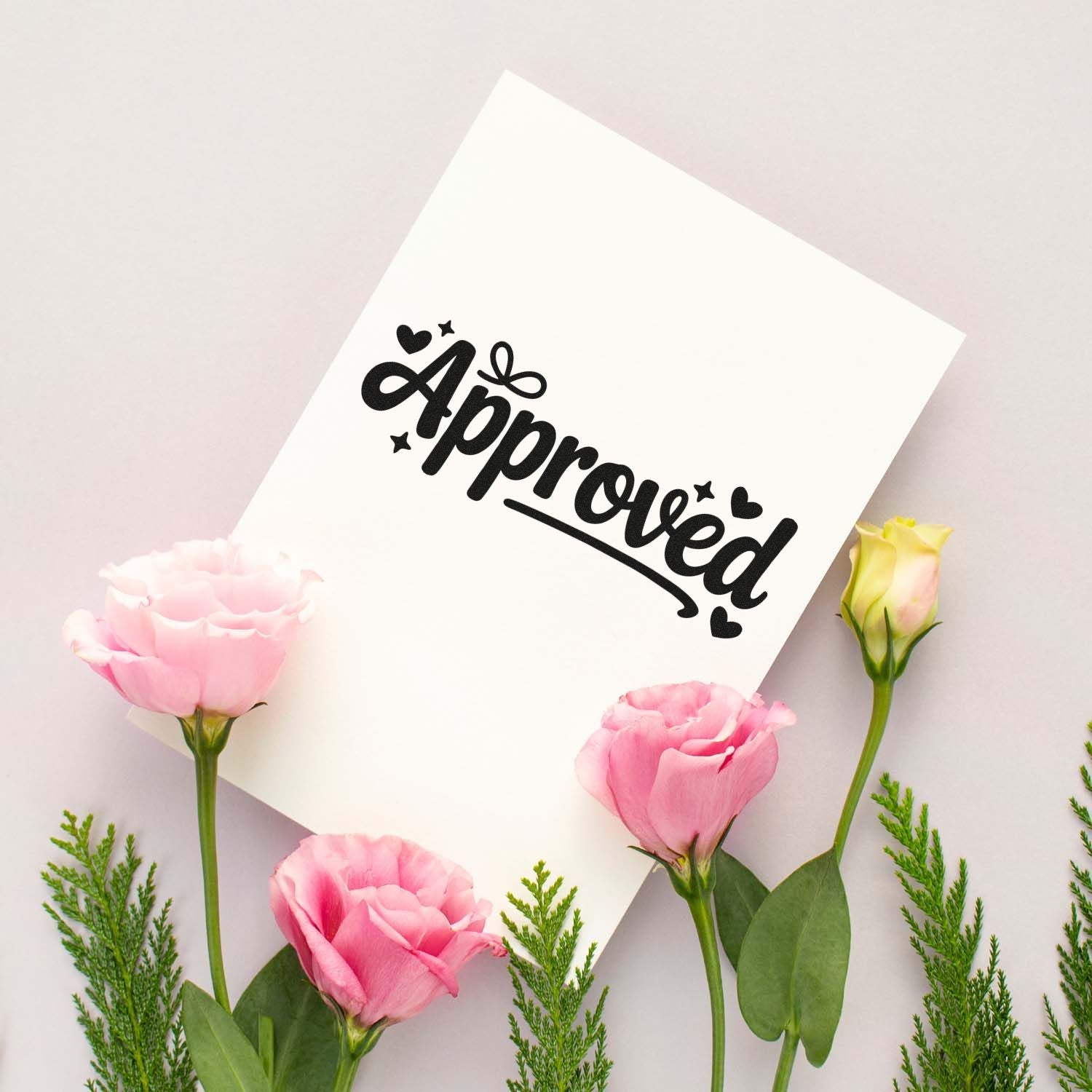 Black Approved stamp and seal on white card, framed by pink flowers and green foliage on a soft pastel background.