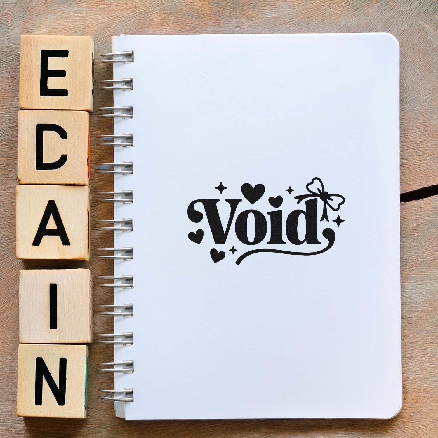 Wooden alphabet stamp blocks beside a white spiral notebook featuring a black decorative Void seal with hearts and butterfly.