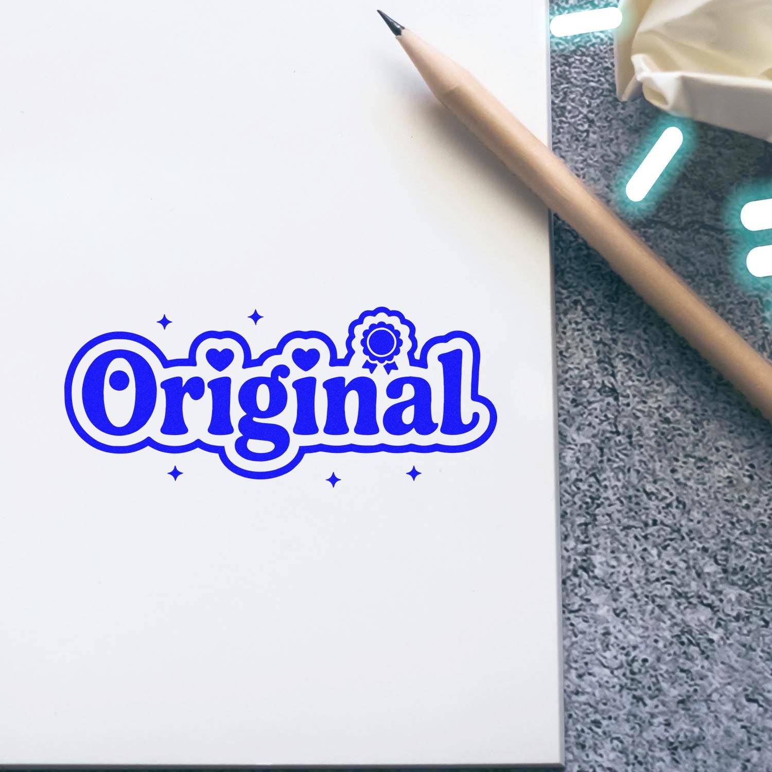 Blue Original stamp seal on white paper beside a beige pencil on a textured gray surface.
