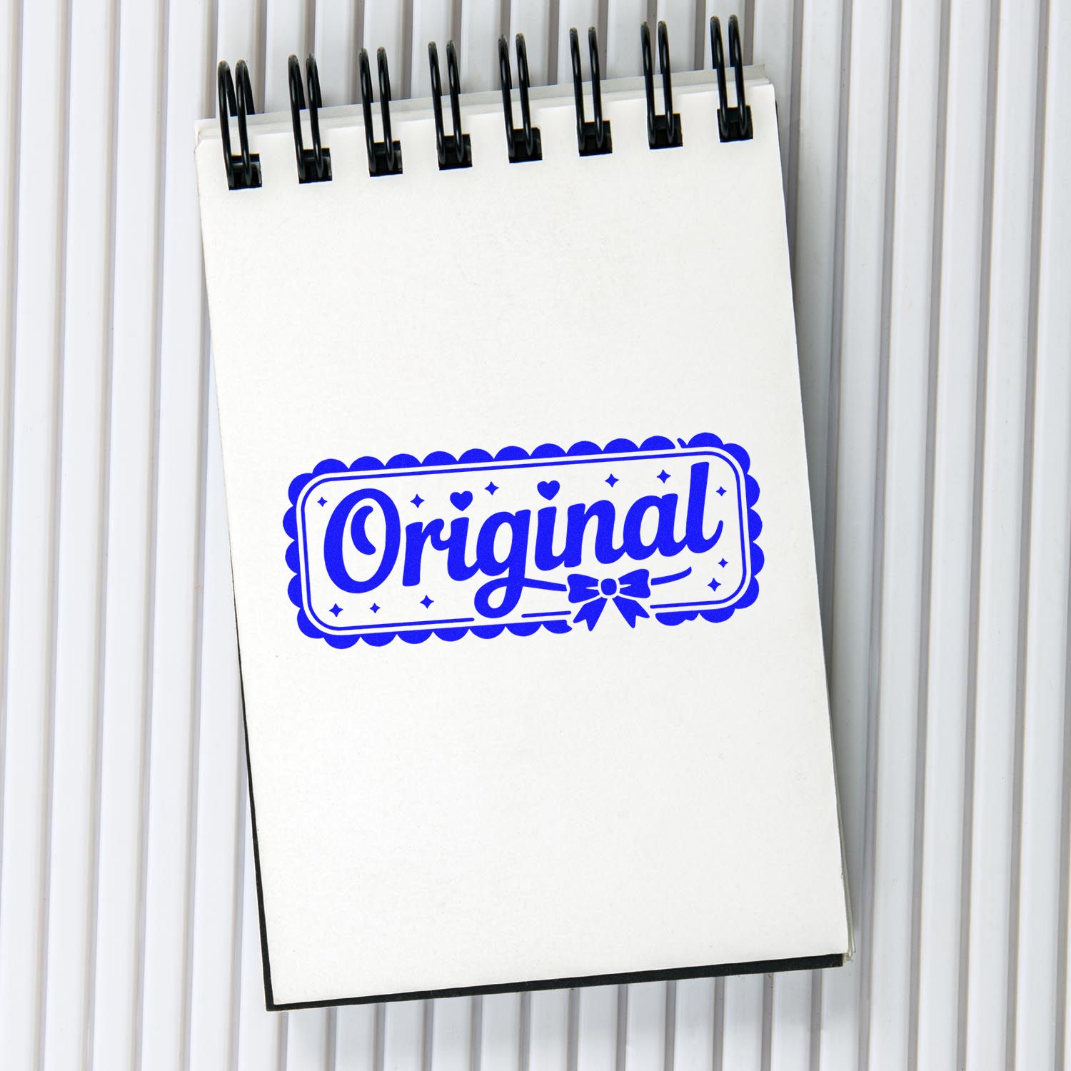 White spiral notepad with a blue Original stamp-style seal and black binding on a light gray striped background.