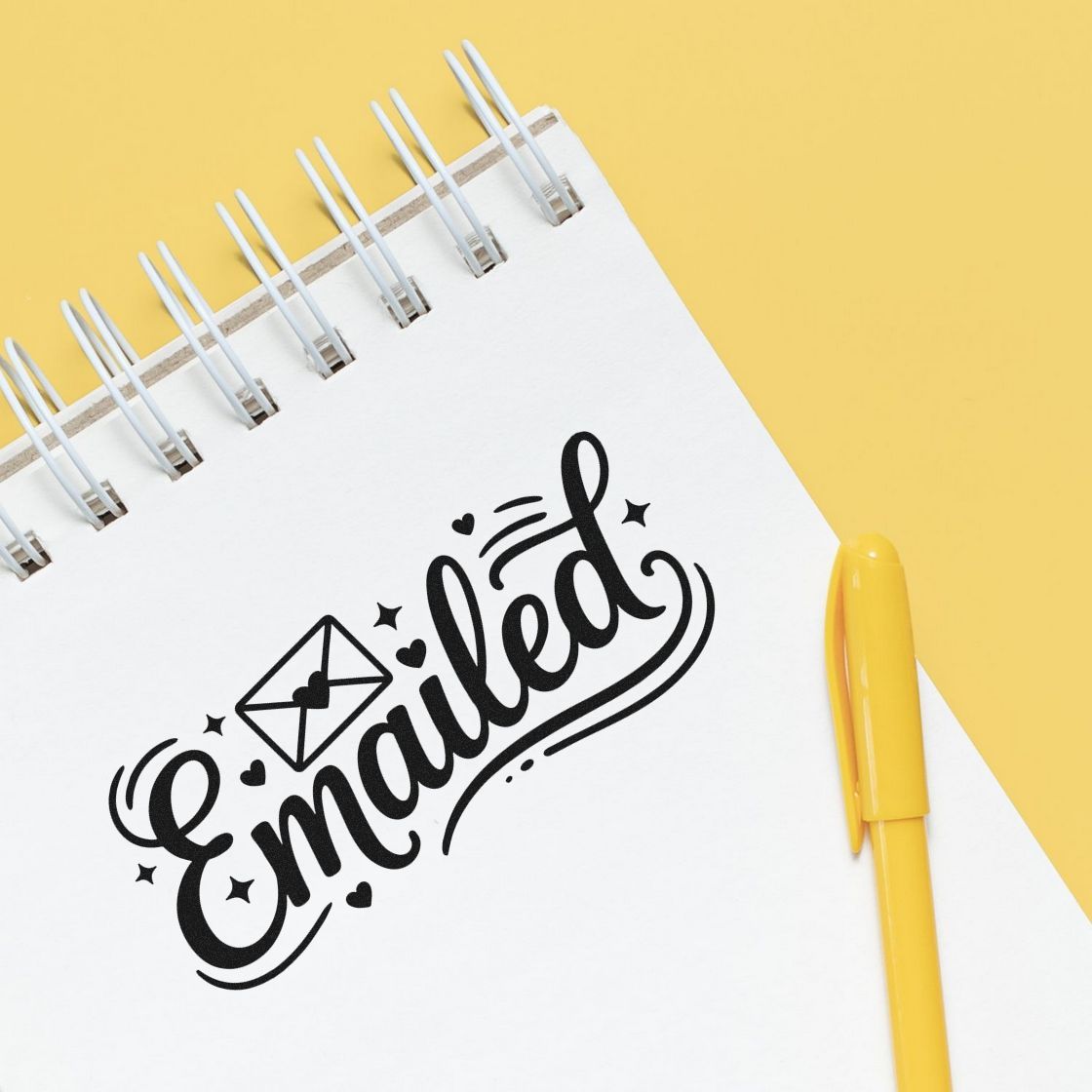 Black Emailed stamp seal on a white spiral notebook with a yellow pen on a bright yellow background.