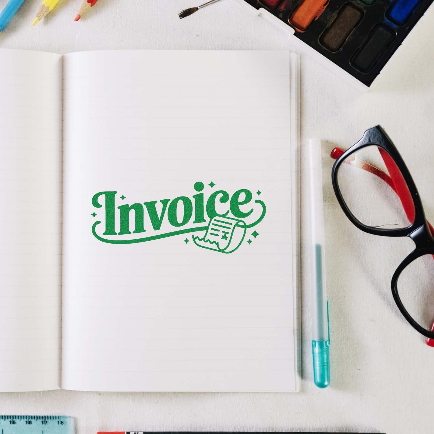 Green custom invoice stamp seal on open notebook, with black glasses, pen, and watercolor tools on a white desk.