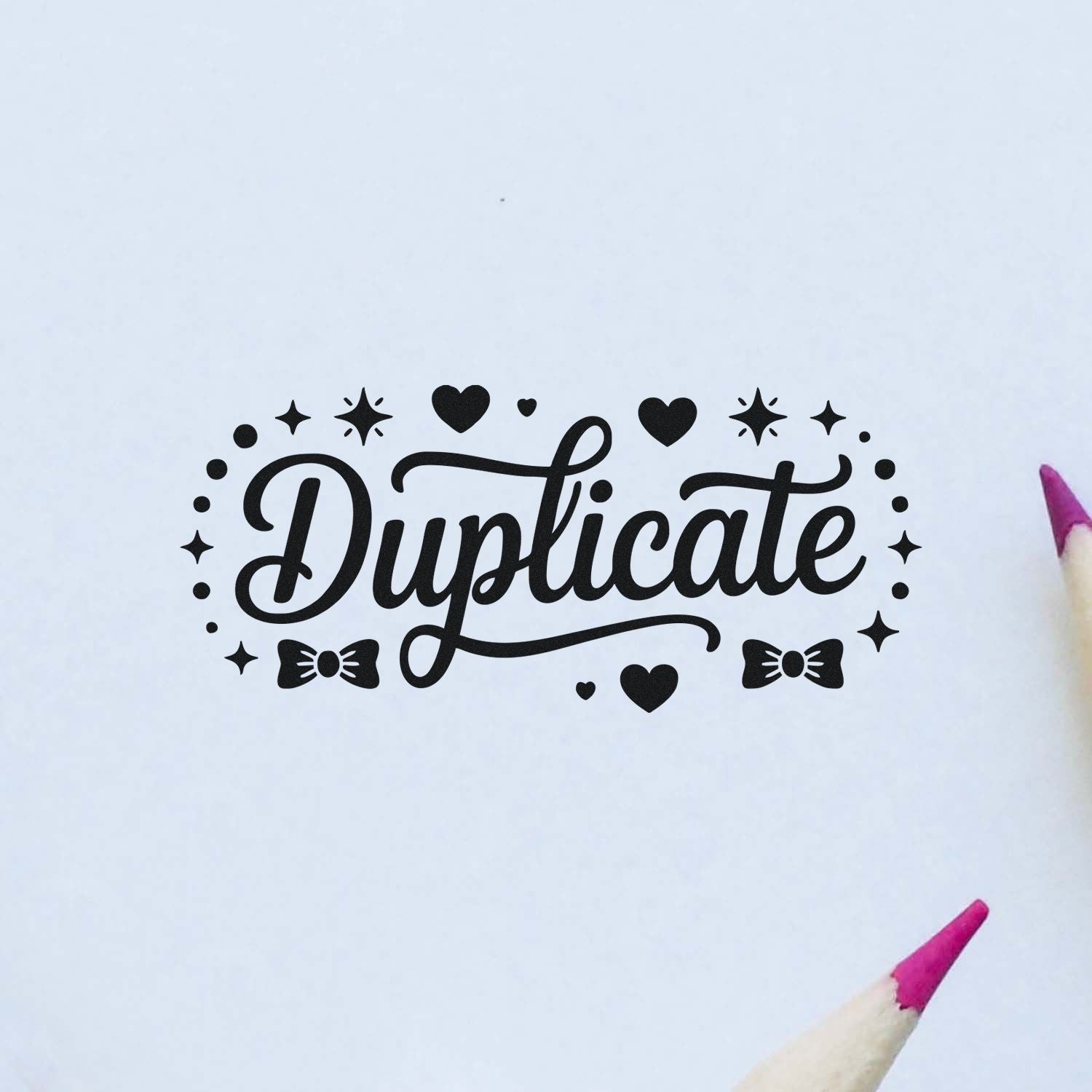 Black Duplicate stamp seal with hearts, stars and bows on white paper, framed by pink pencil tips.