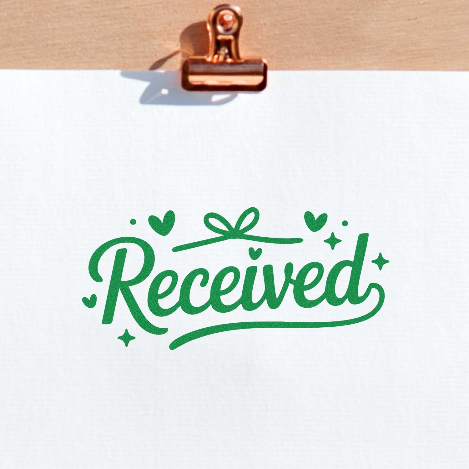 Copper clip holding paper with green Received stamp seal, hearts, and stars on white paper.