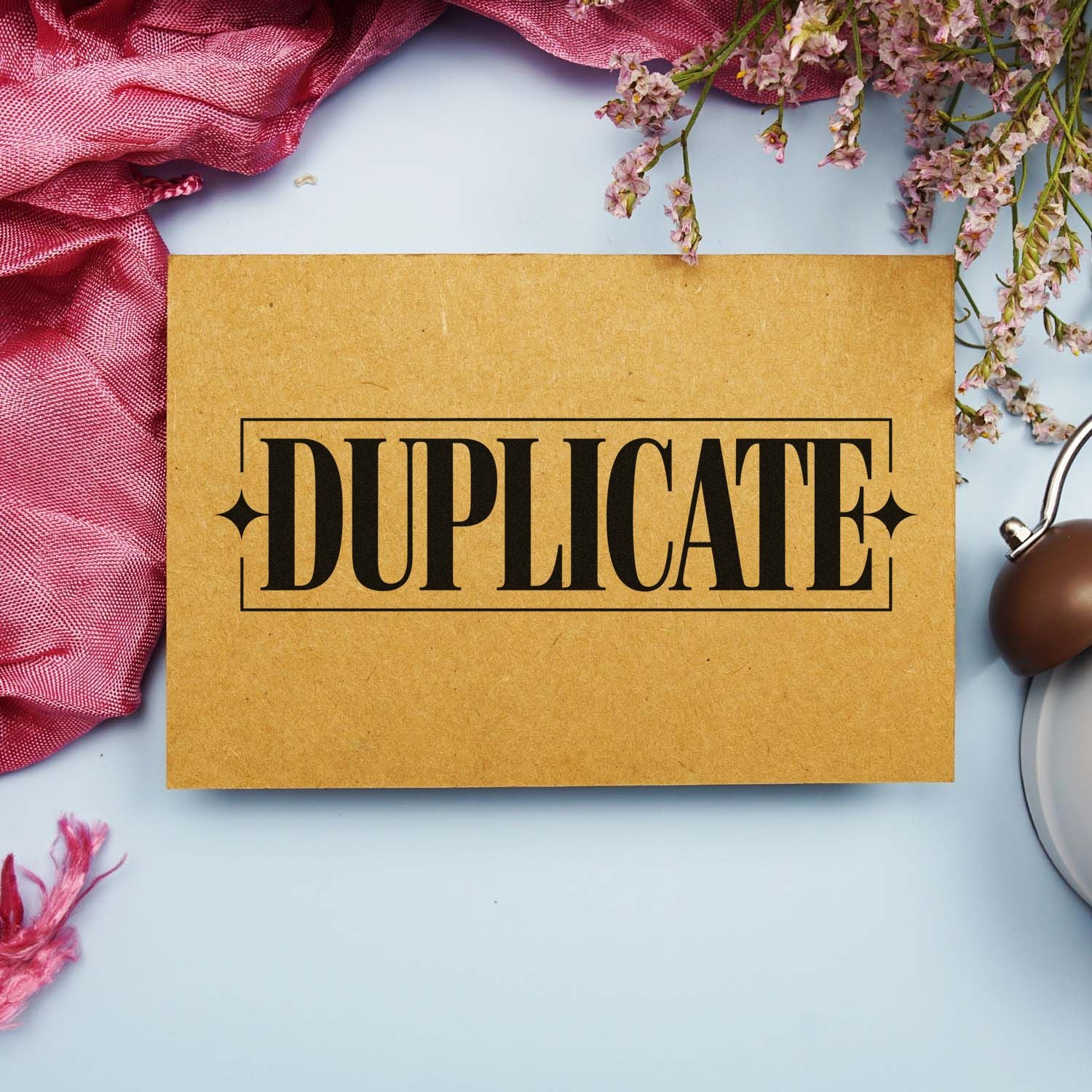 Kraft paper card stamped DUPLICATE in black, with pink fabric, dried flowers, and a brown seal stamp beside it.