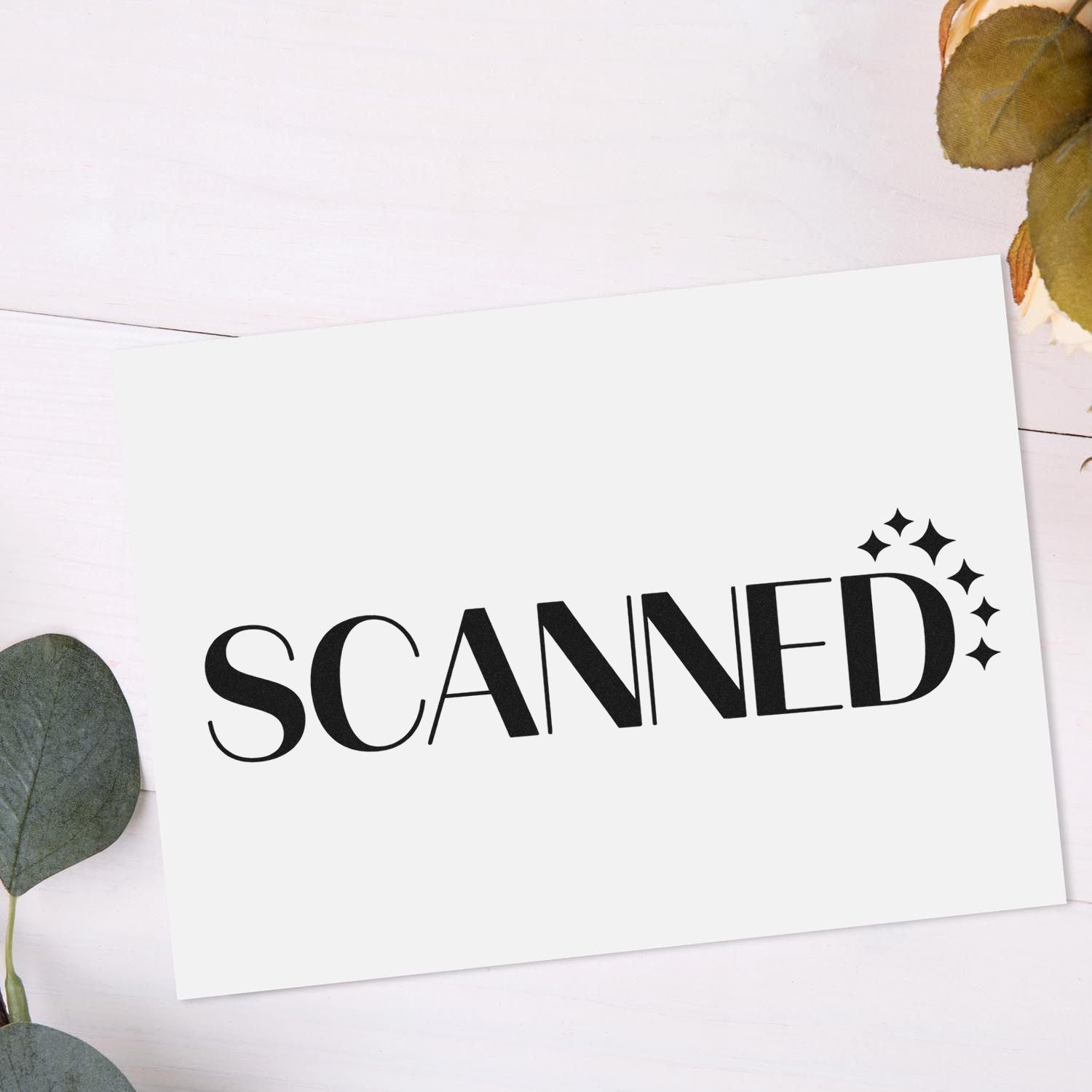 White stamp and seal card with bold black SCANNED text and sparkle icons, accented by eucalyptus leaves.