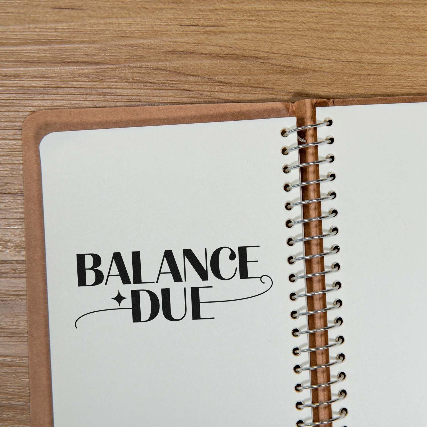 Black Balance Due stamp and seal on a spiral-bound notebook with brown cover on a wood table.