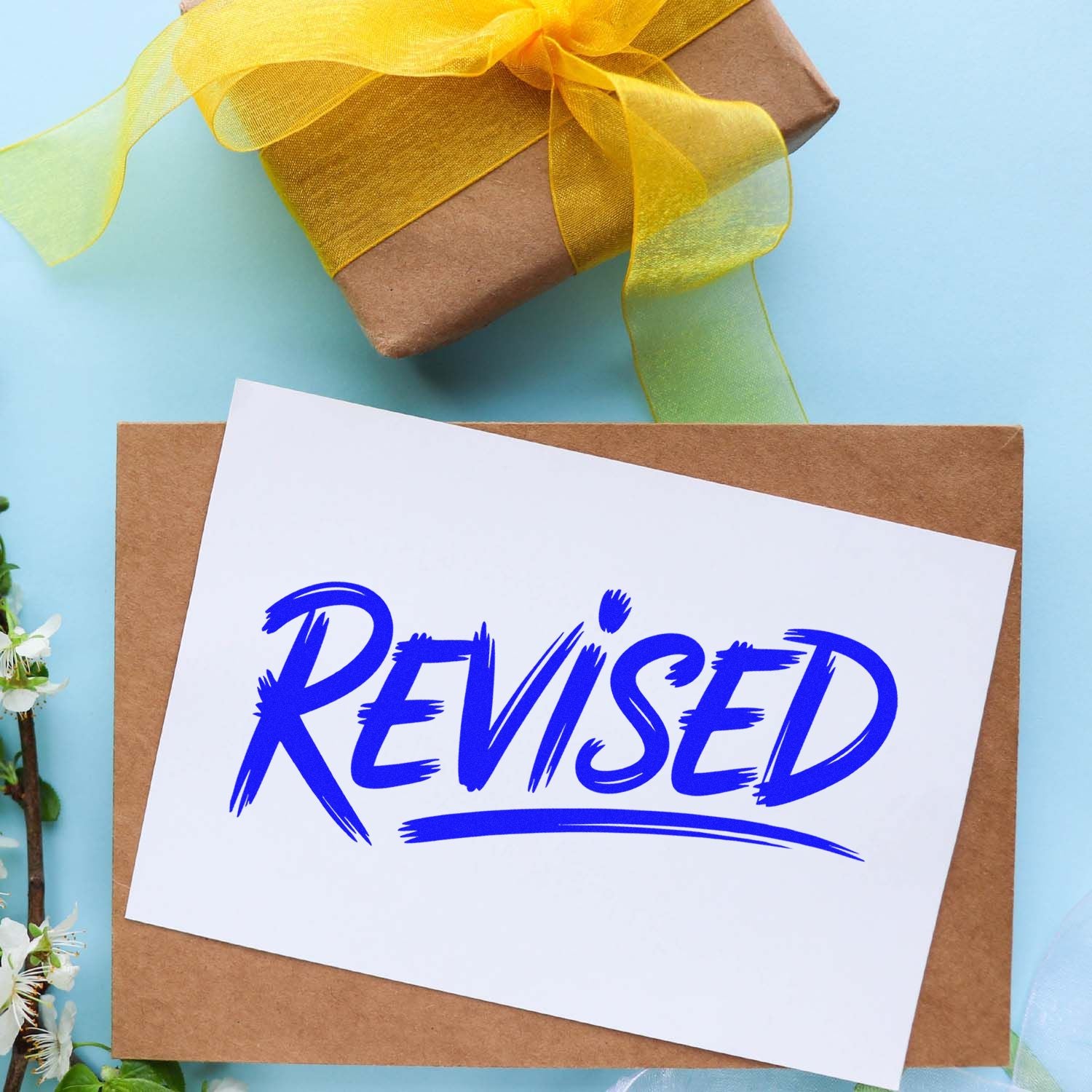 Blue Revised stamp seal on white paper over kraft envelope, beside a yellow ribbon gift box on light blue background.