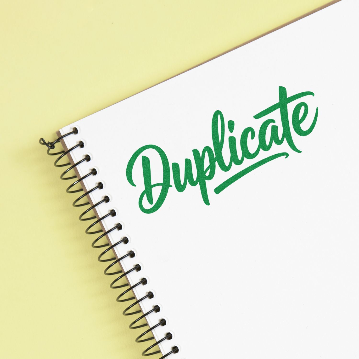White spiral-bound notebook with green Duplicate stamp and seal on pale yellow background.