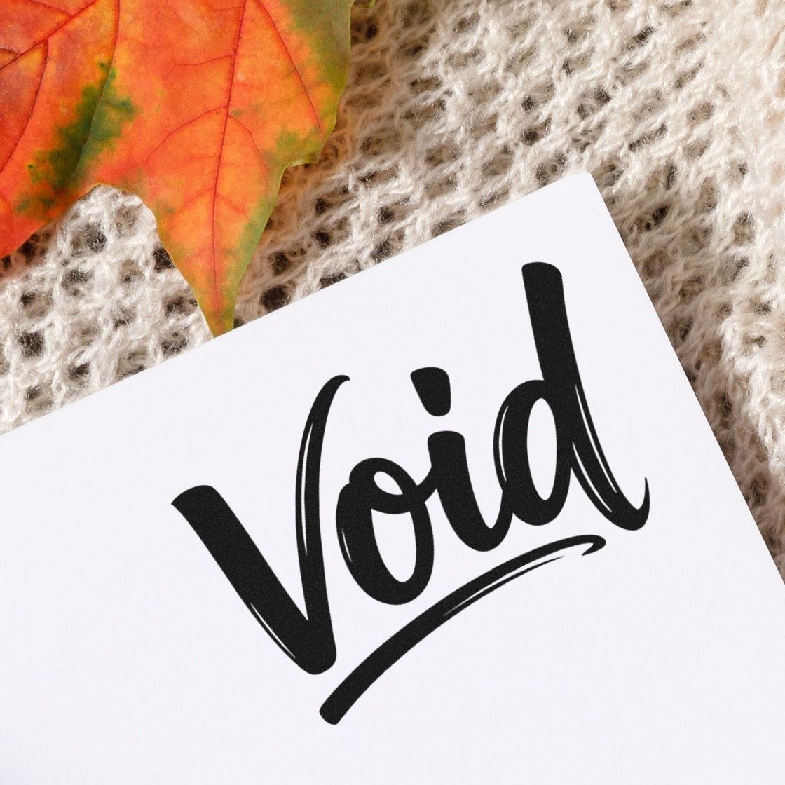 Black Void stamp seal on white paper, with autumn leaf on beige knitted fabric background.