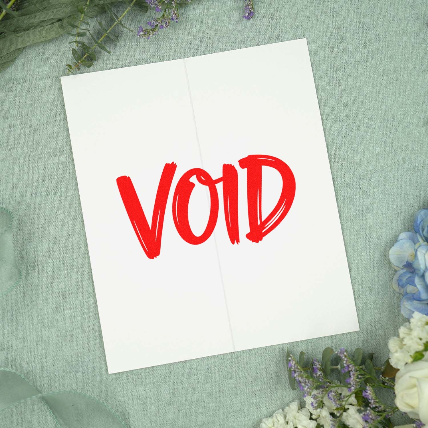 Red VOID stamp seal on white folded card, set on mint fabric with pastel flowers.