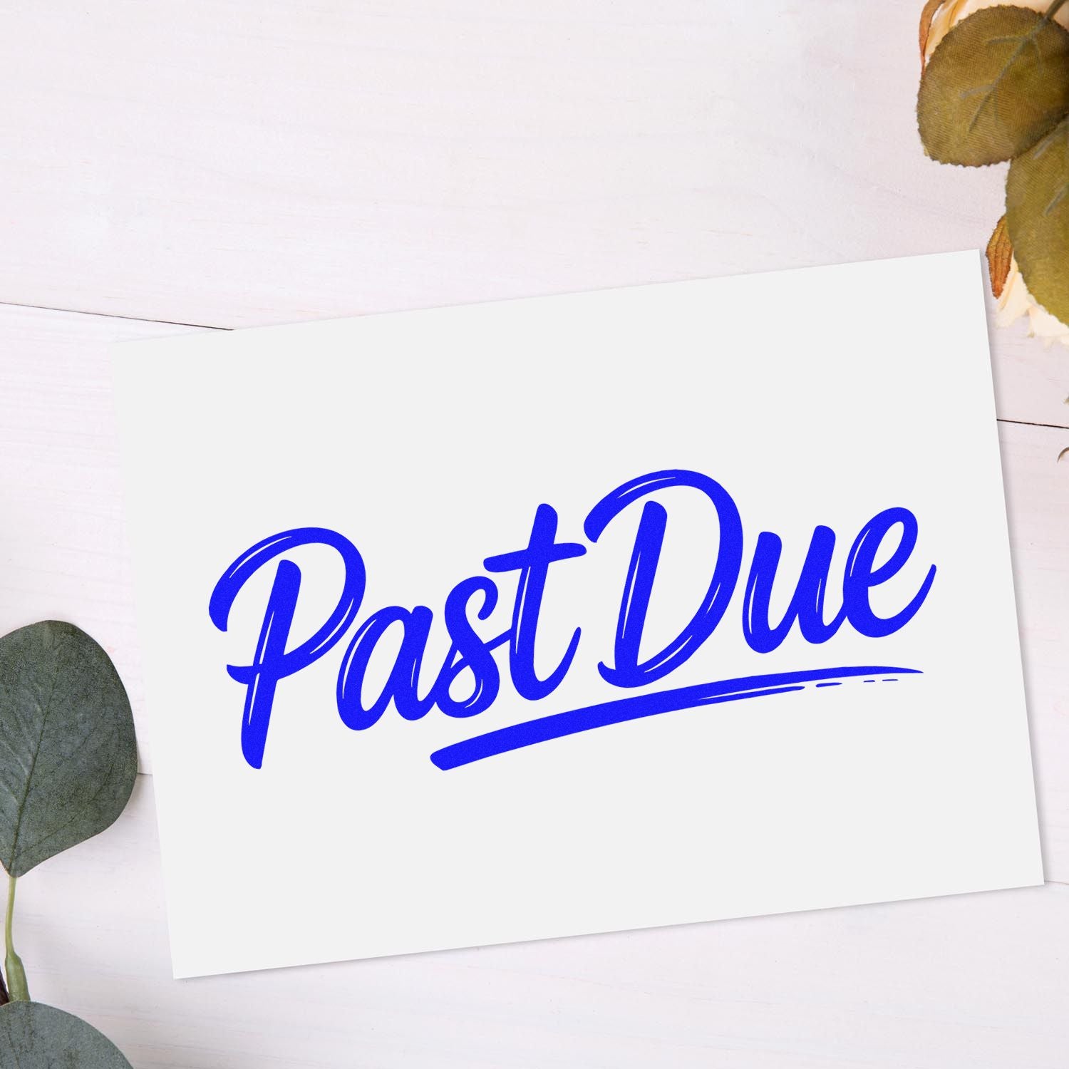 White card with bold blue Past Due stamp seal, accented by dried eucalyptus leaves on a pale wood background.