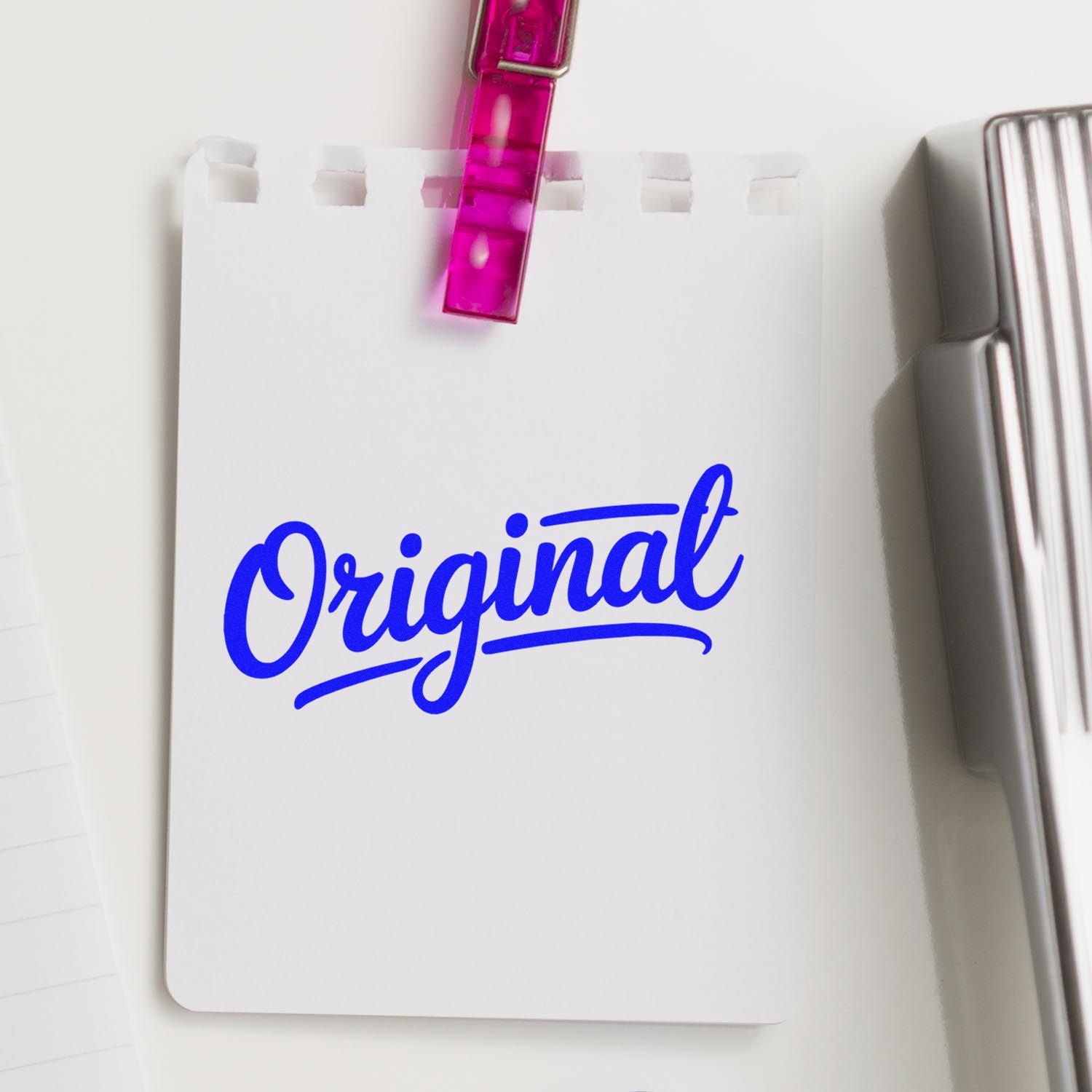 Custom stamp and seal product with blue Original logo on white card, clipped by pink acrylic clip, silver stamp beside it.