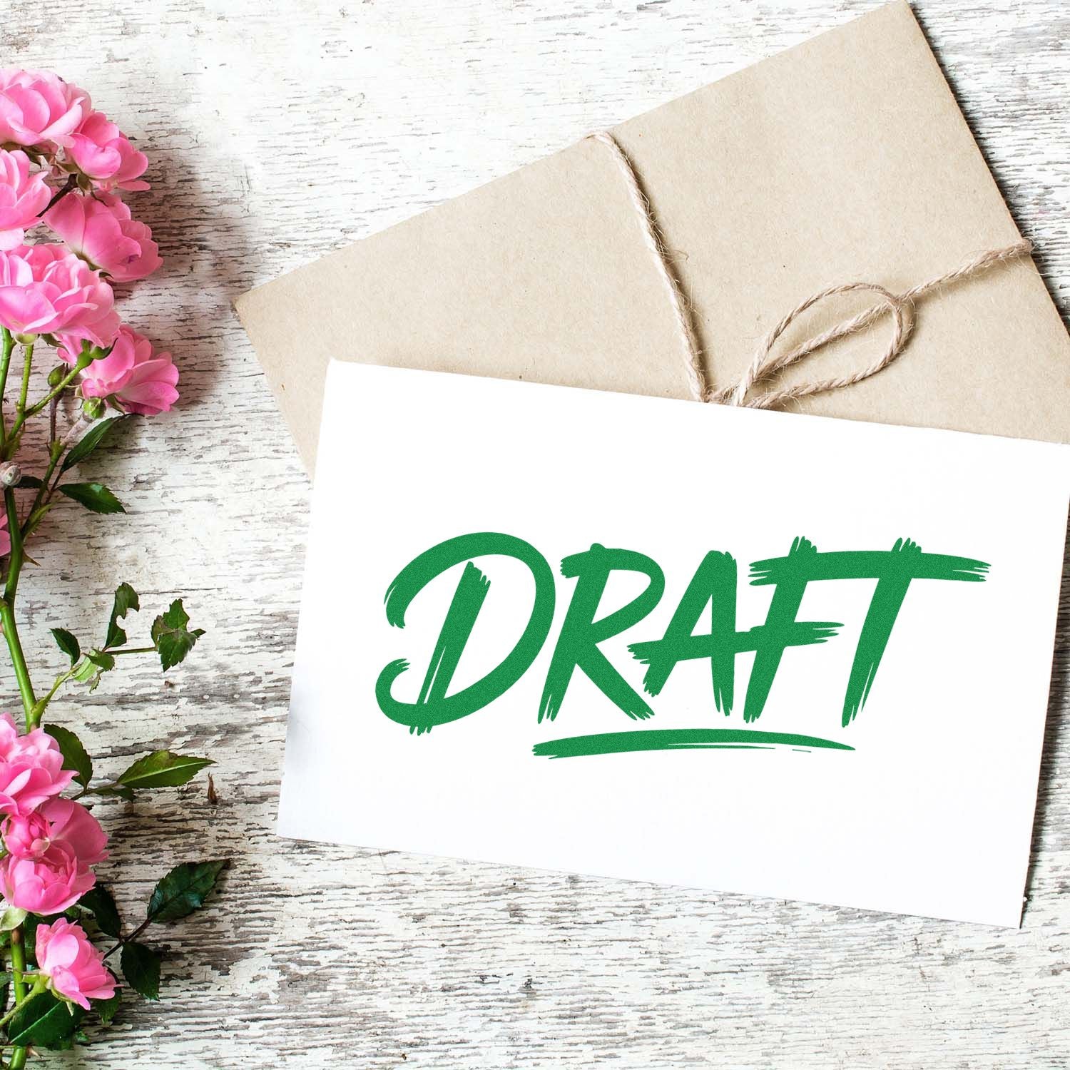 Green draft stamp and seal design on white card, with kraft envelope, twine, and pink flowers on rustic wood.
