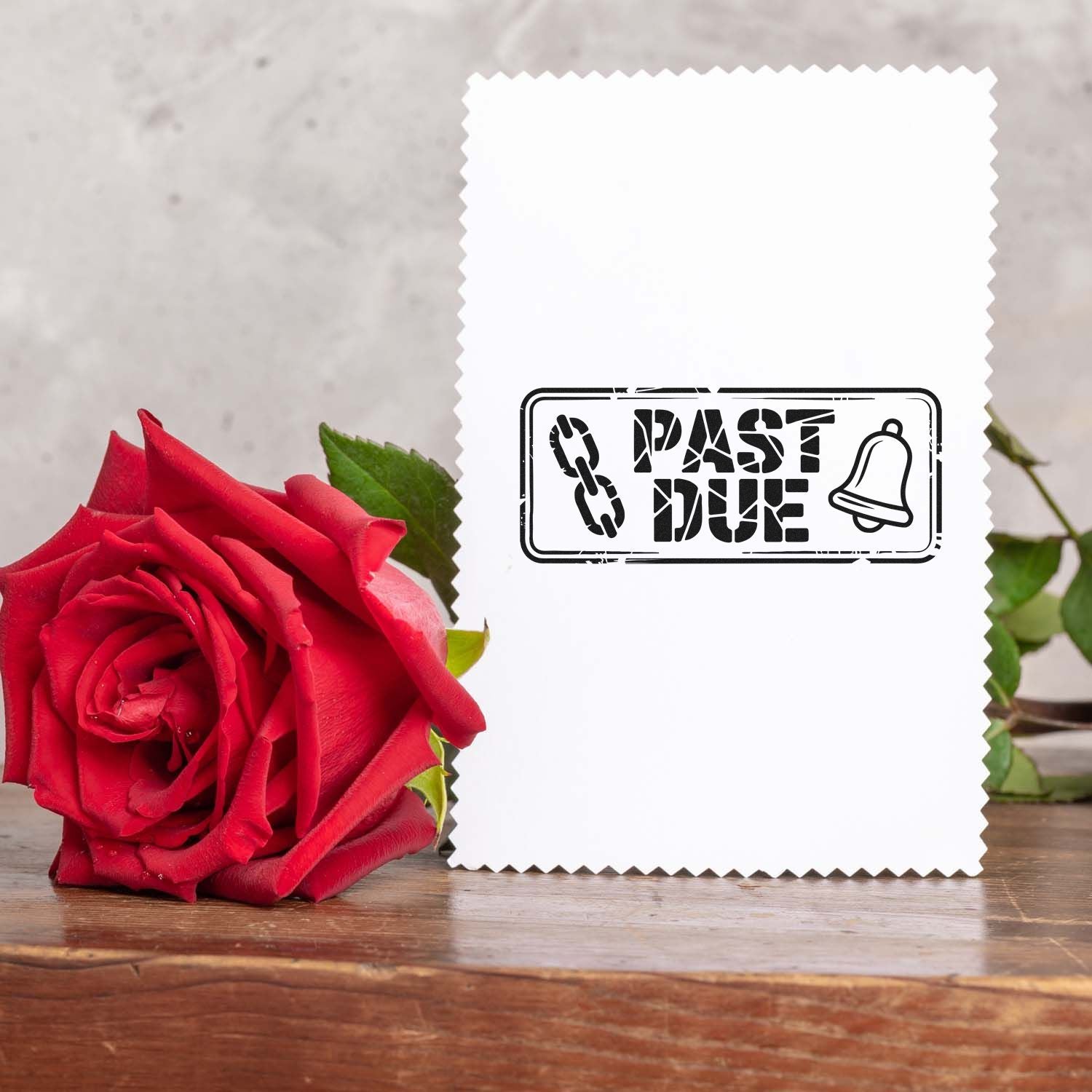 White scalloped stamp and seal card with black PAST DUE bell mark, beside a red rose on wood.
