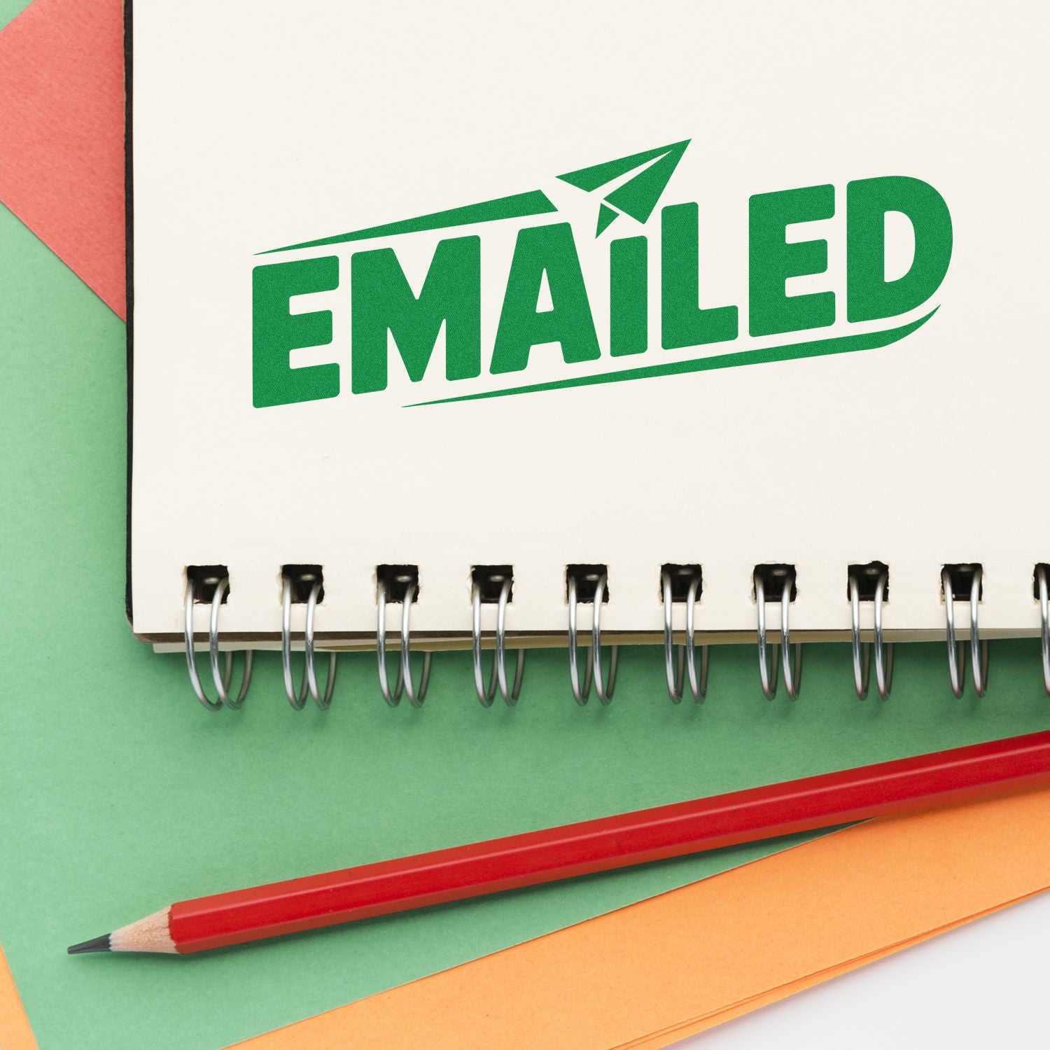 Green EMAILED stamp seal on white spiral notebook with red pencil and colorful paper sheets