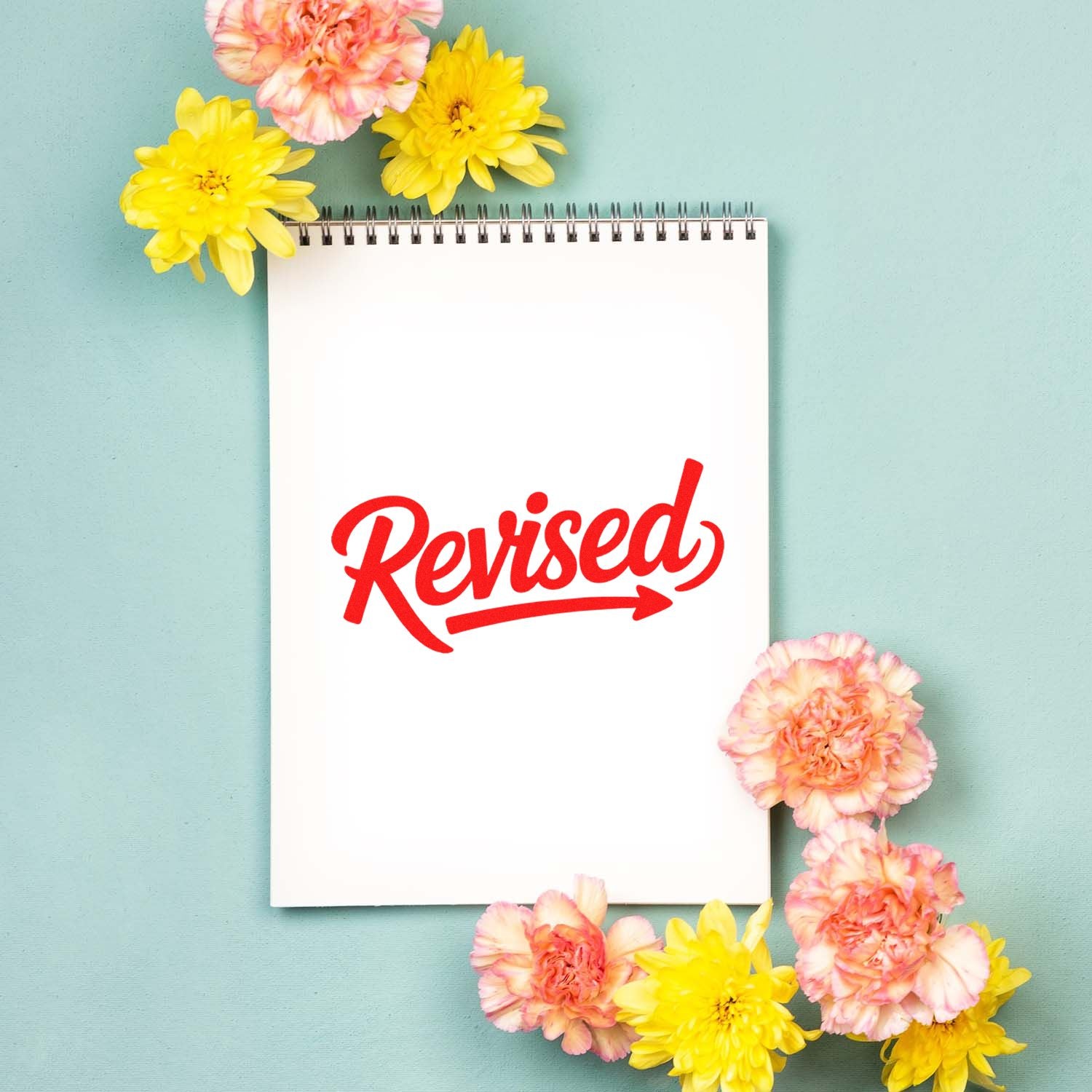 Red Revised rubber stamp on white spiral notebook, framed by yellow and pink flowers on a mint background.
