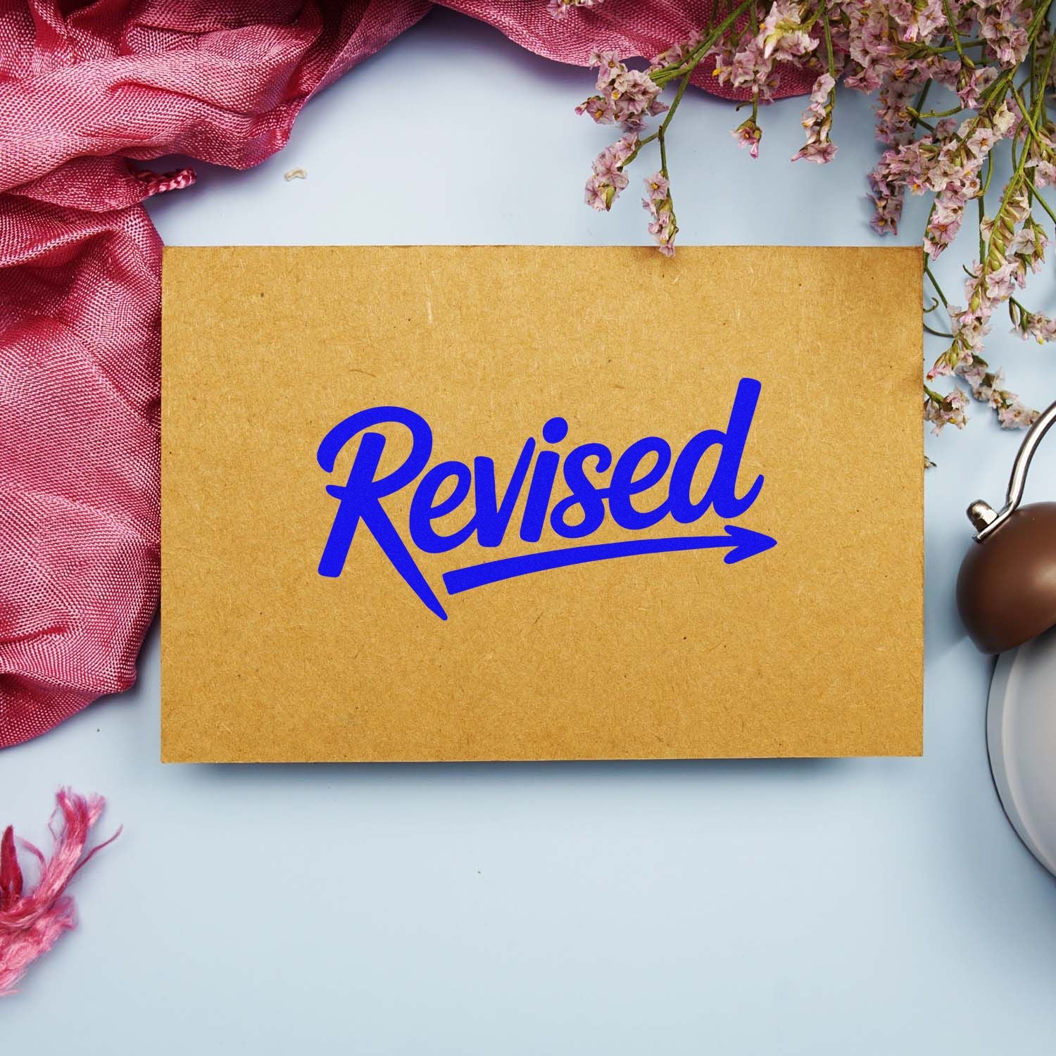 Blue Revised stamp on kraft paper, with pink fabric, dried flowers, and a brown wax seal on a pale blue background.