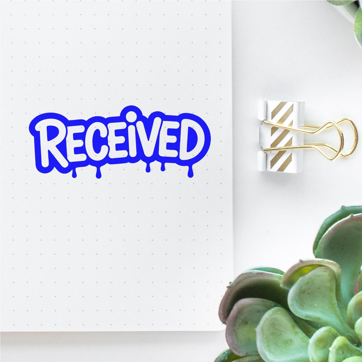 Blue RECEIVED stamp beside gold-striped binder clip seal on dotted notebook page